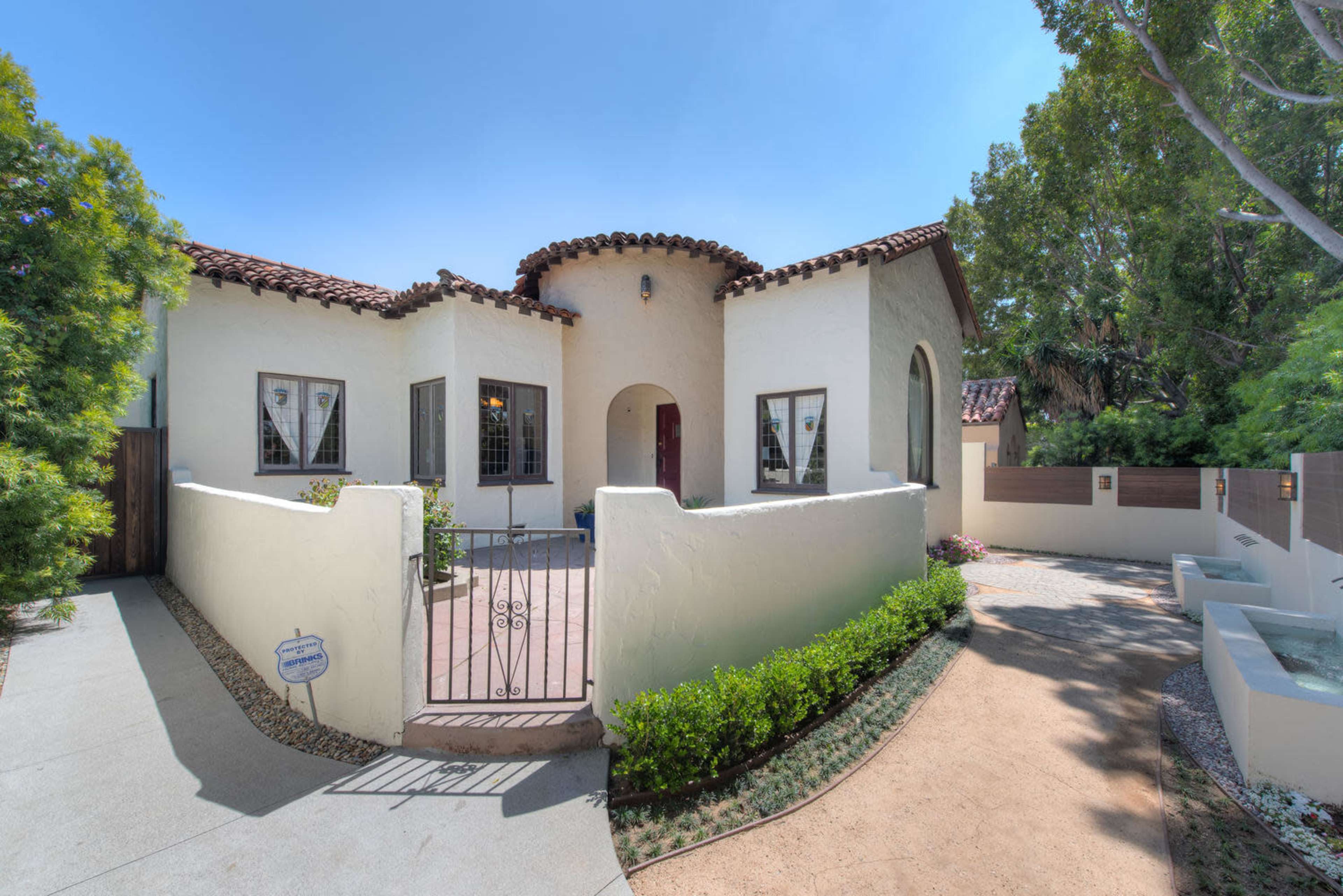 A single-story house with a stucco exterior, a tile roof, and a gated entrance surrounded by landscaped pathways.