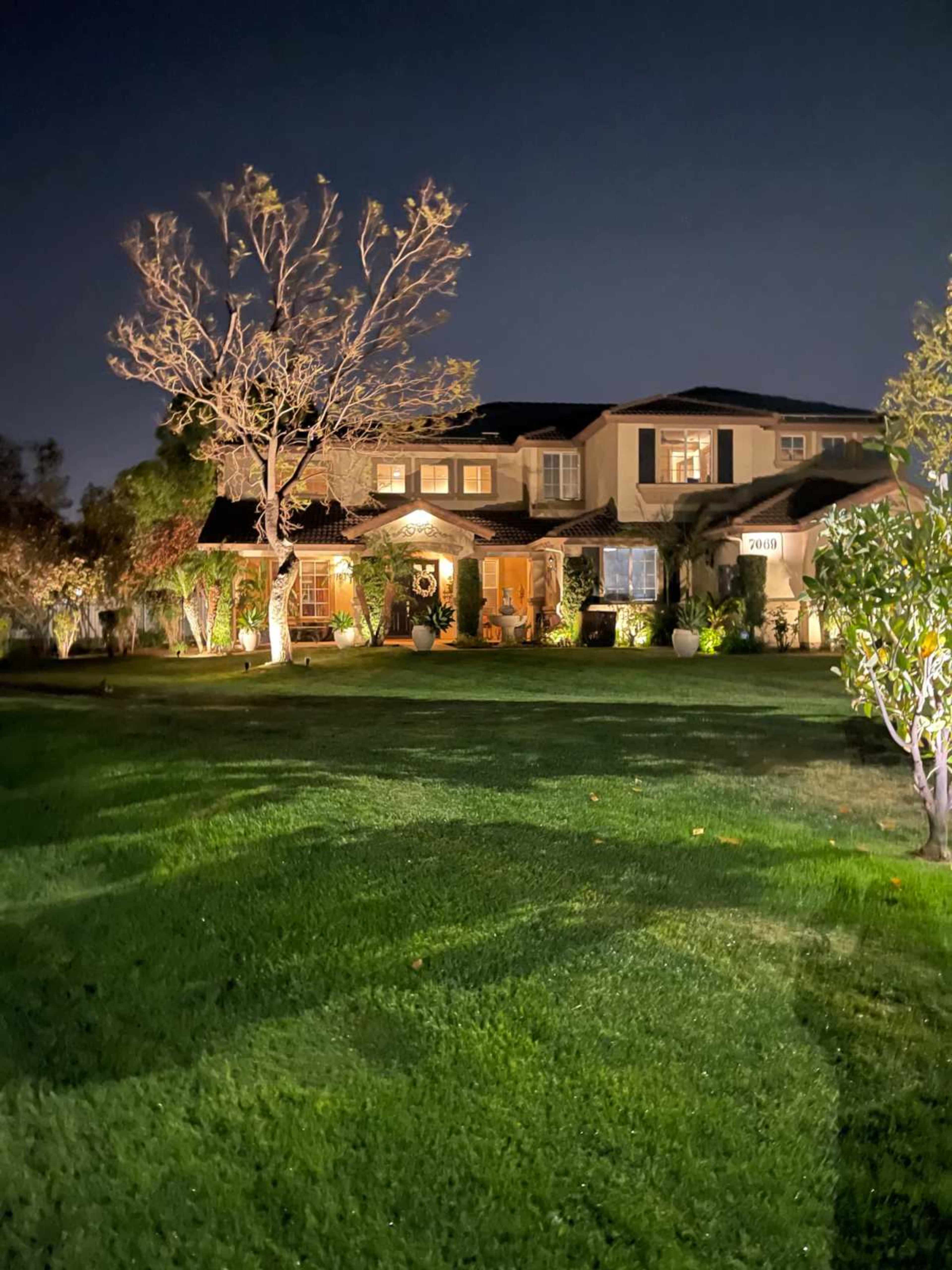 A well-lit house with a manicured lawn and trees is visible at night.