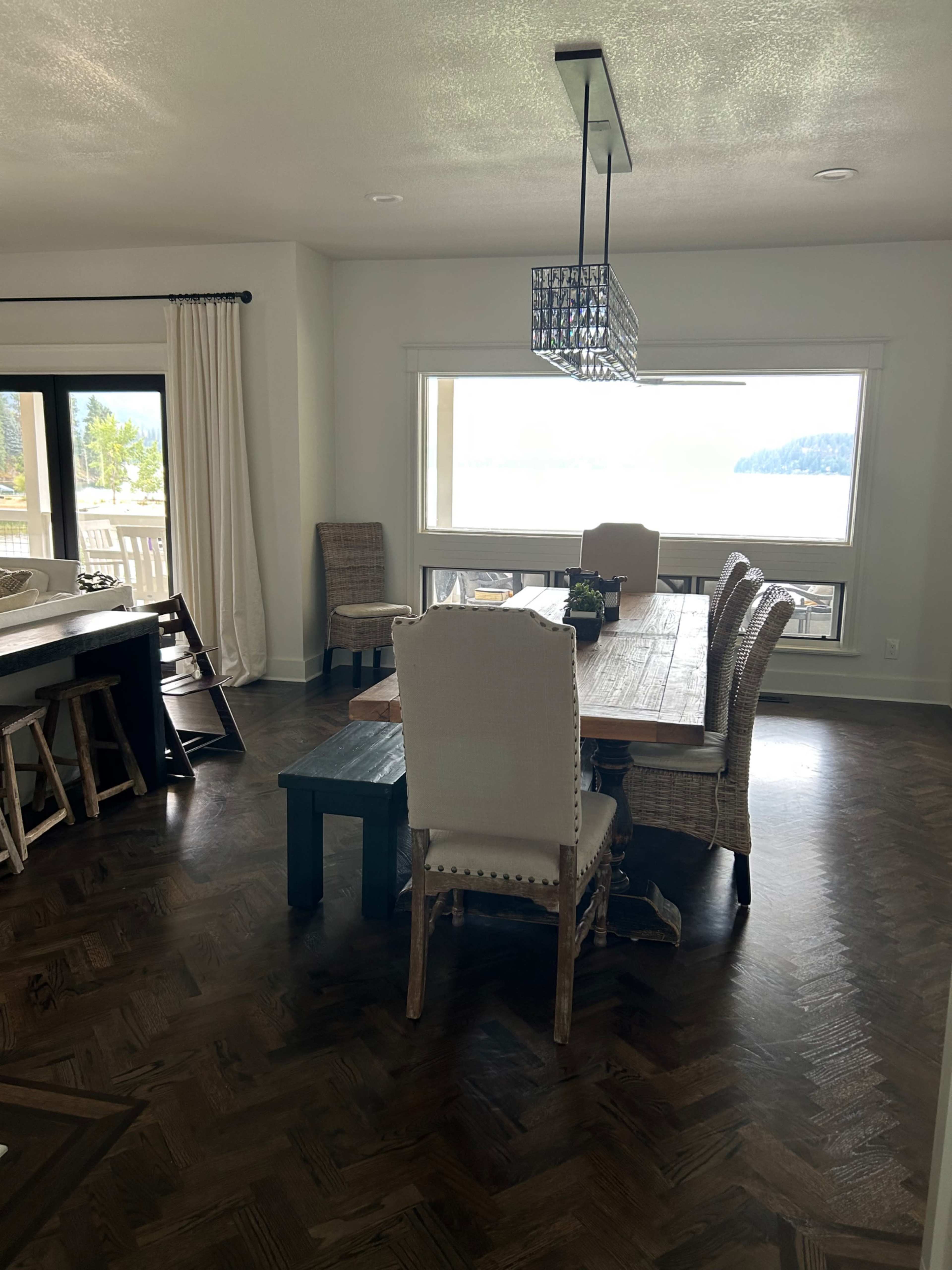 A dining area featuring a wooden table surrounded by upholstered and woven chairs, with a large window revealing a scenic view of the outdoors.