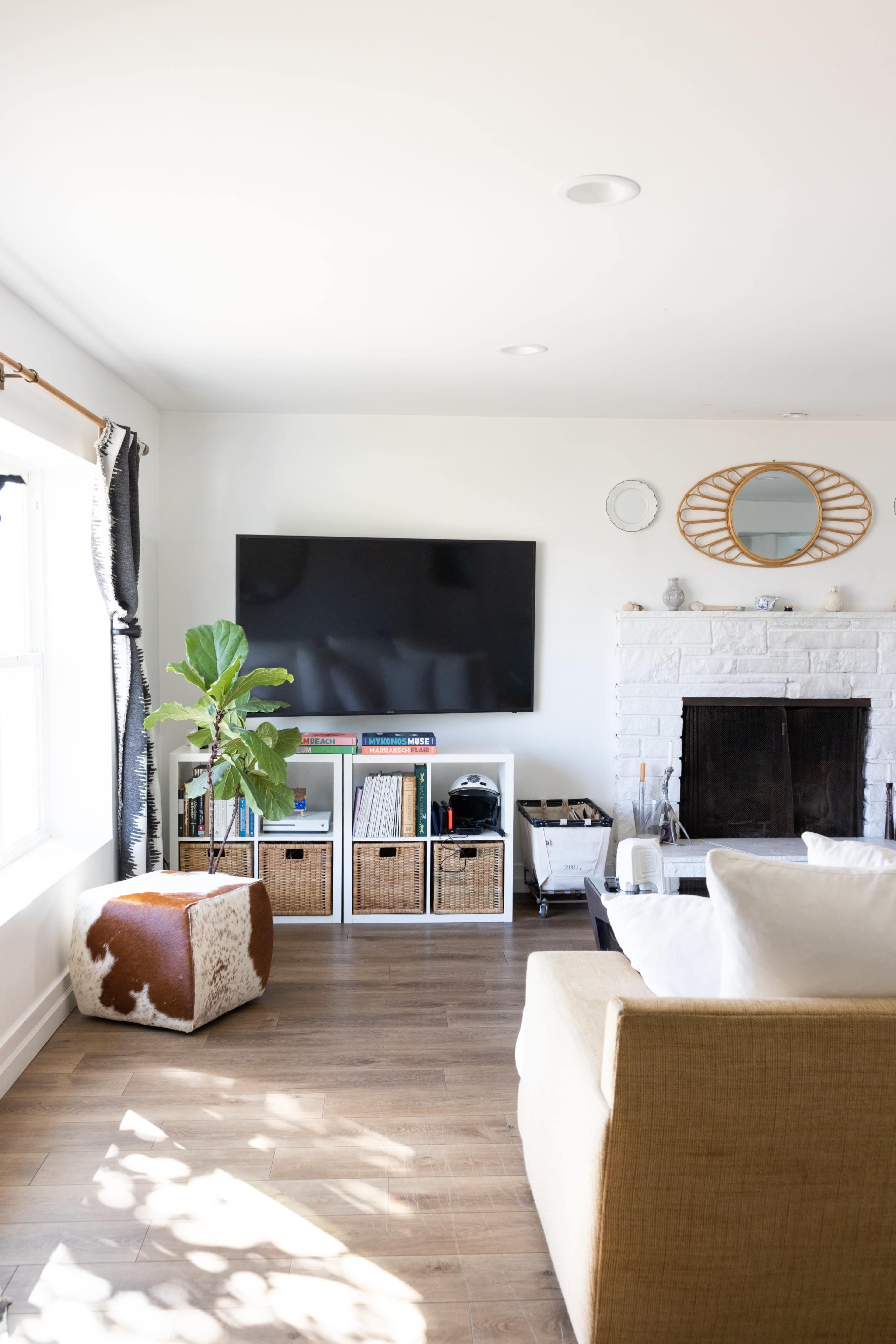 A bright living room with a mounted television, a fireplace, wicker storage boxes, and a decorative plant.