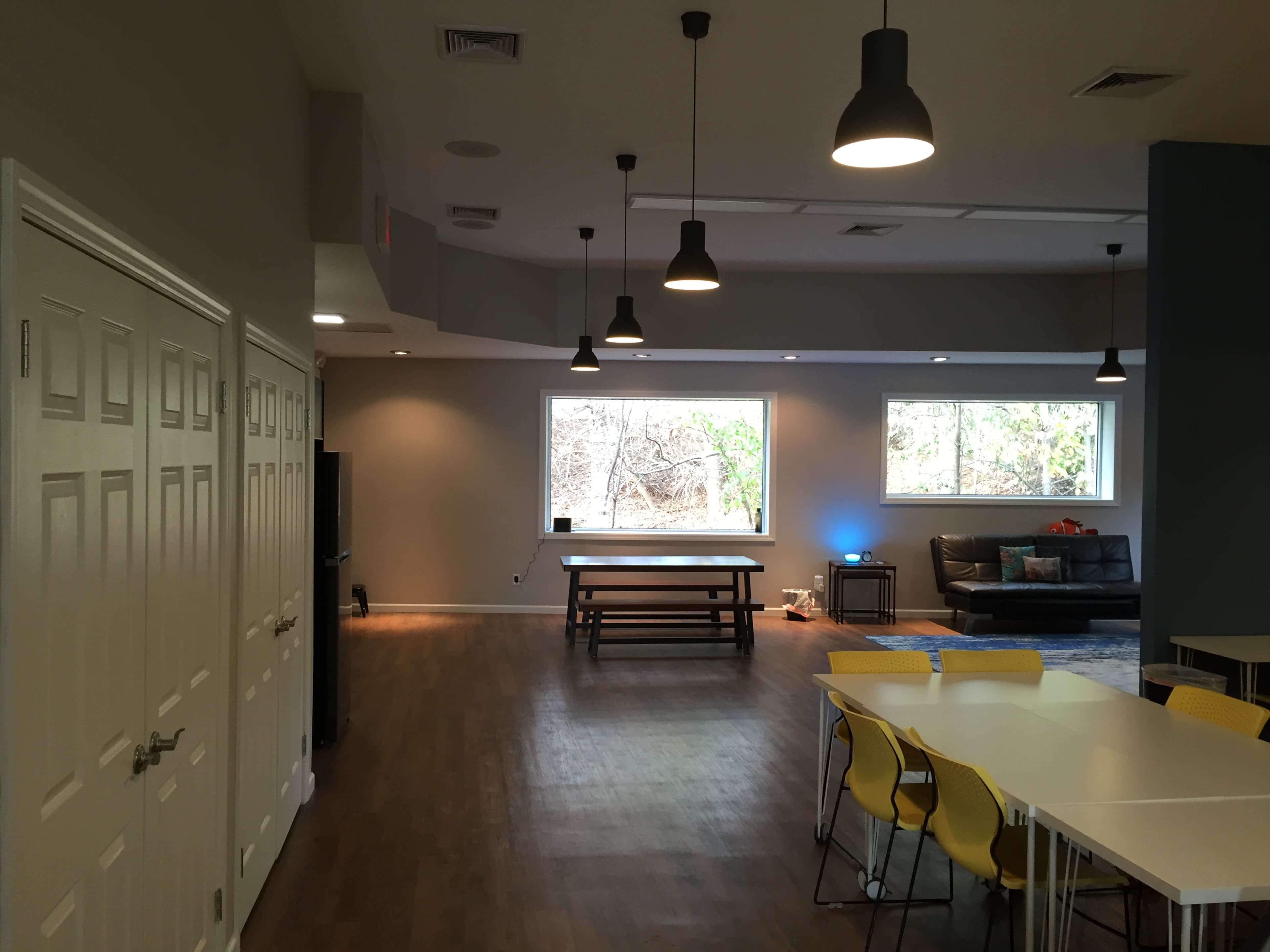 A spacious, modern room with a dining table, seating area, and bright windows overlooking a wooded area.