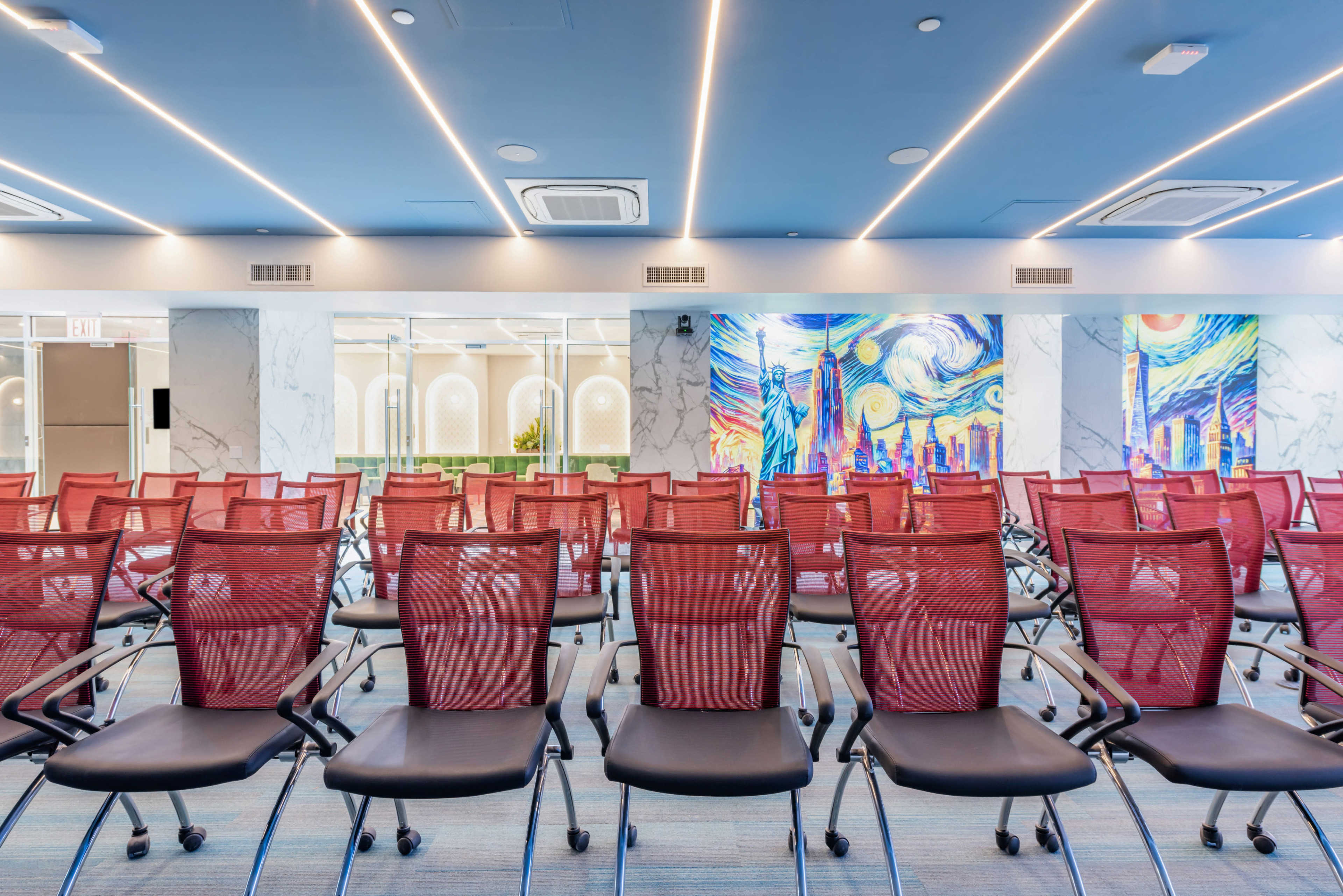 The image shows a modern conference room with rows of red mesh chairs facing colorful wall murals.