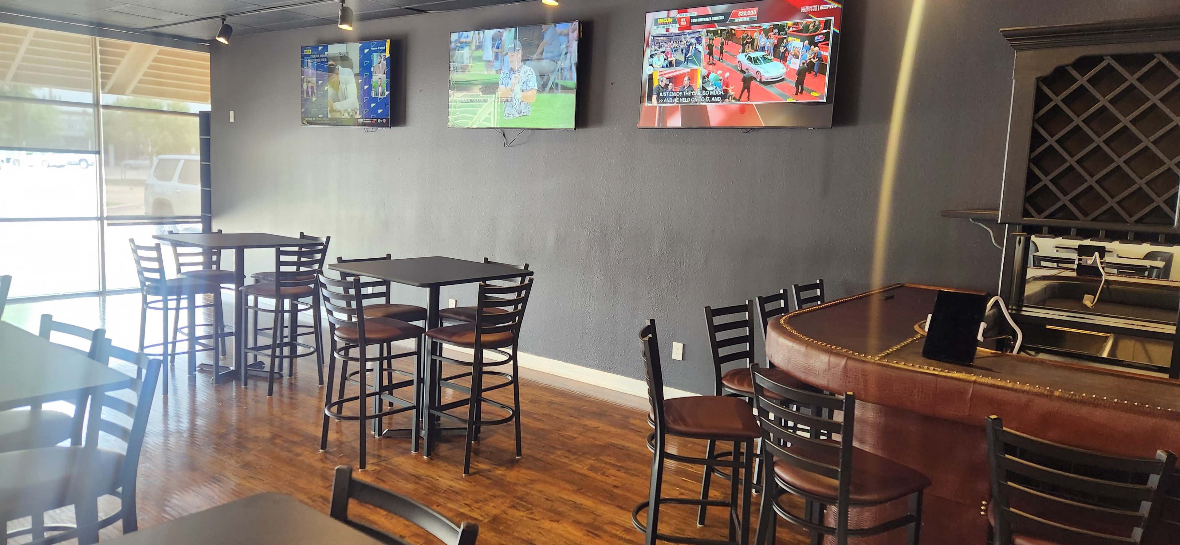 The image shows a sports bar interior with several tables and chairs, featuring multiple screens displaying sports events on the walls.
