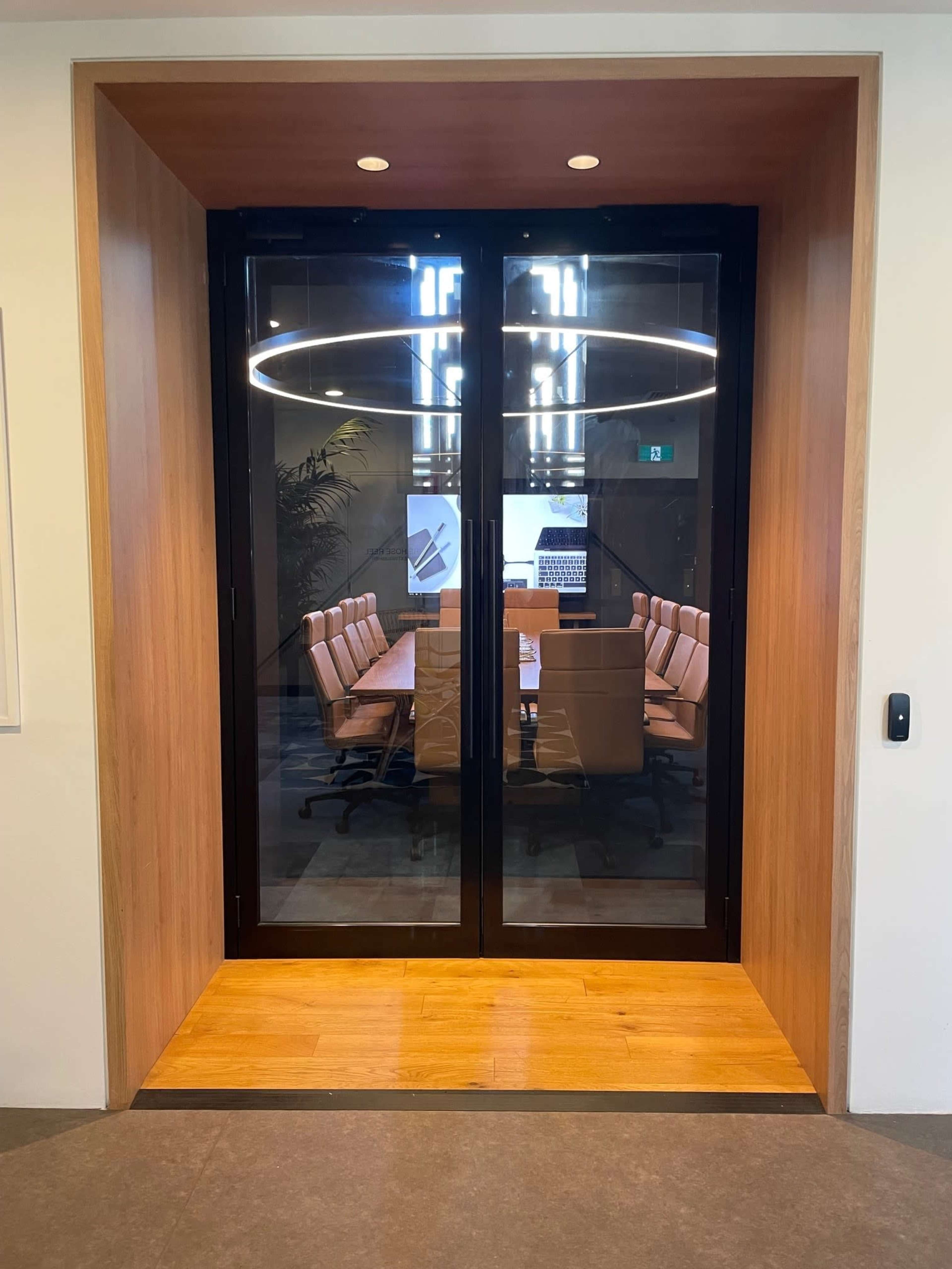 The image shows a glass door opening to a modern conference room with a long table and several chairs.