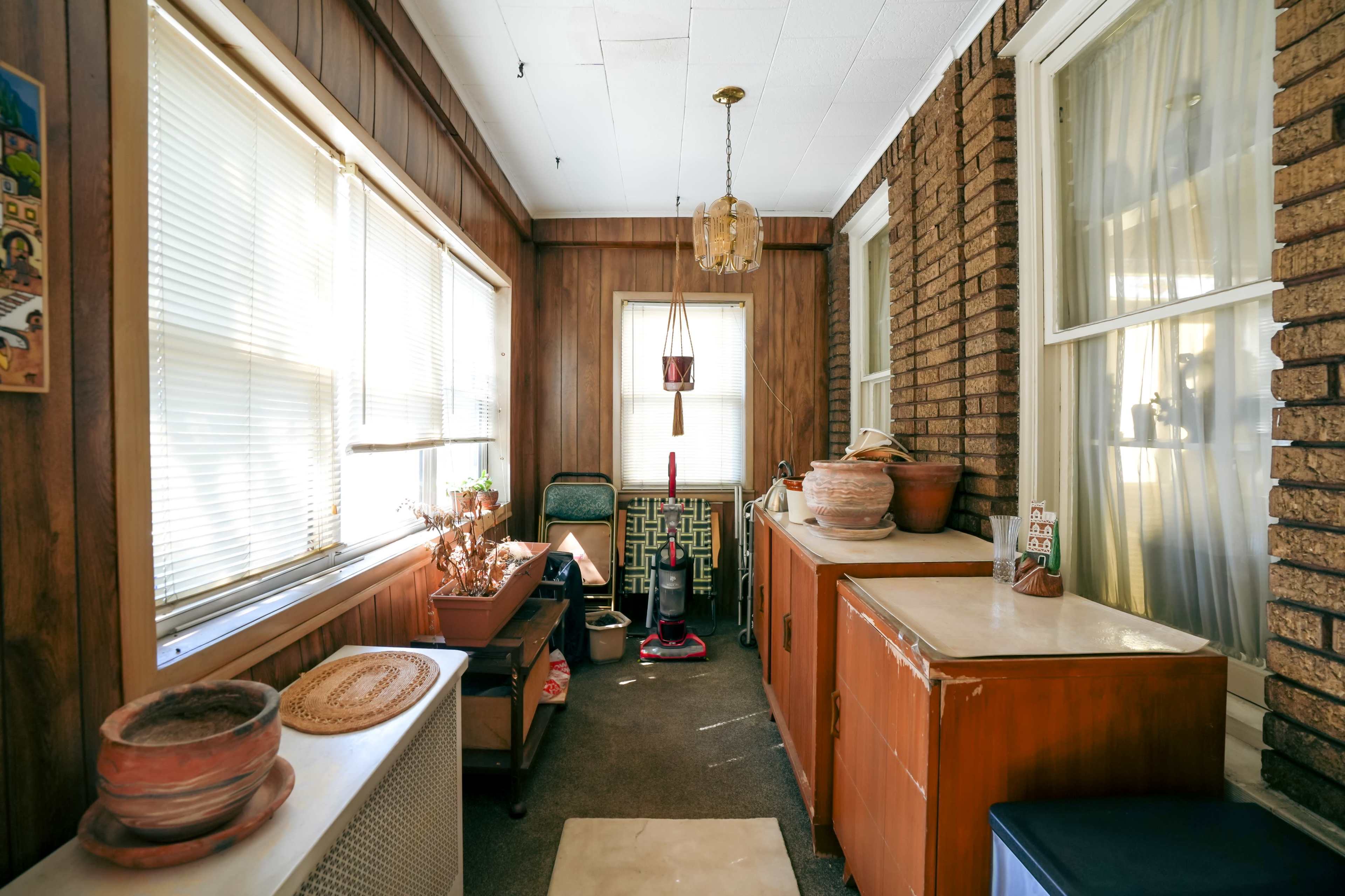 A narrow sunroom with wooden paneling, large windows, and several pot plants along the walls.