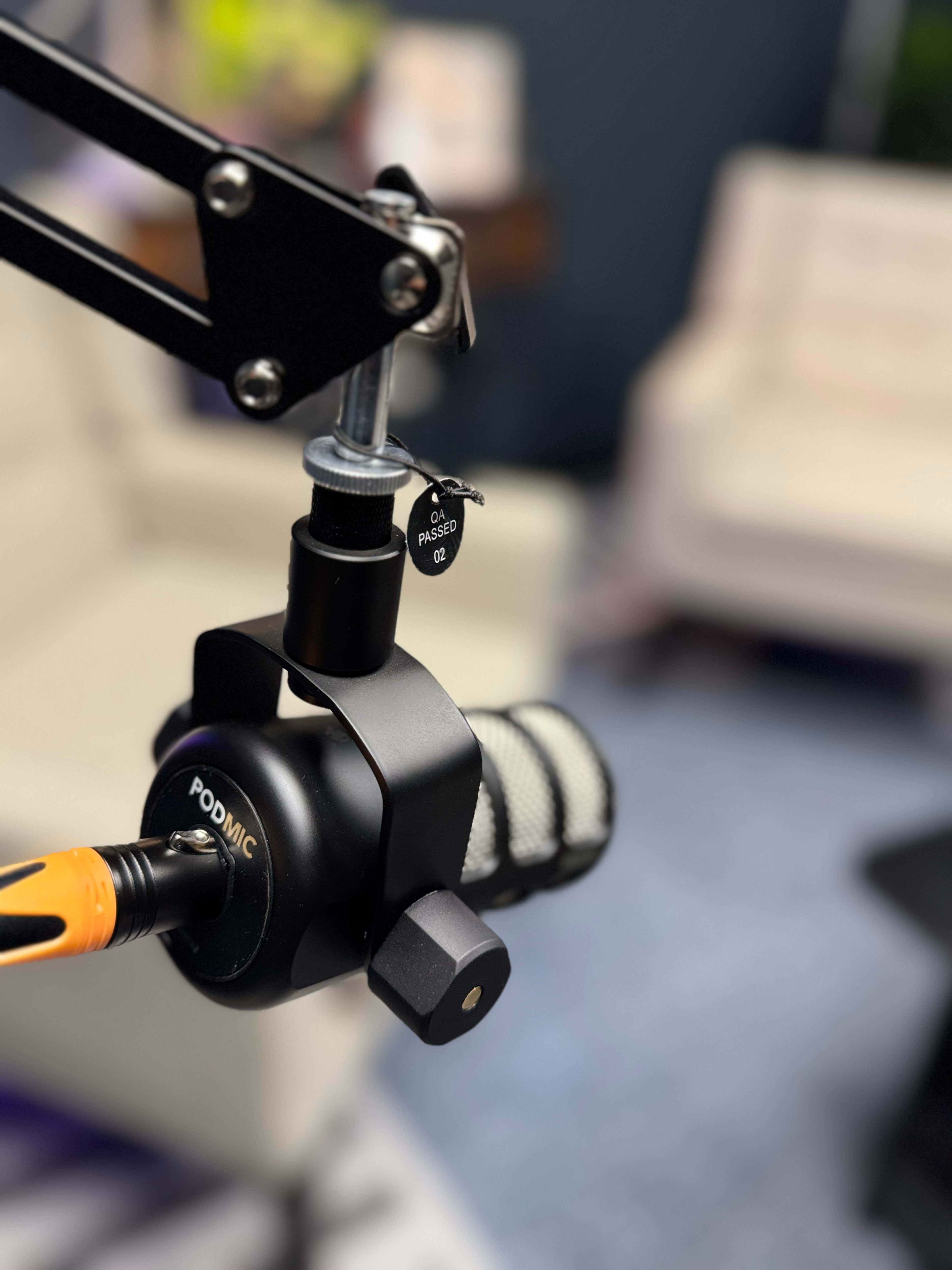 A black microphone with a shock mount is mounted on an adjustable arm in a well-lit room.