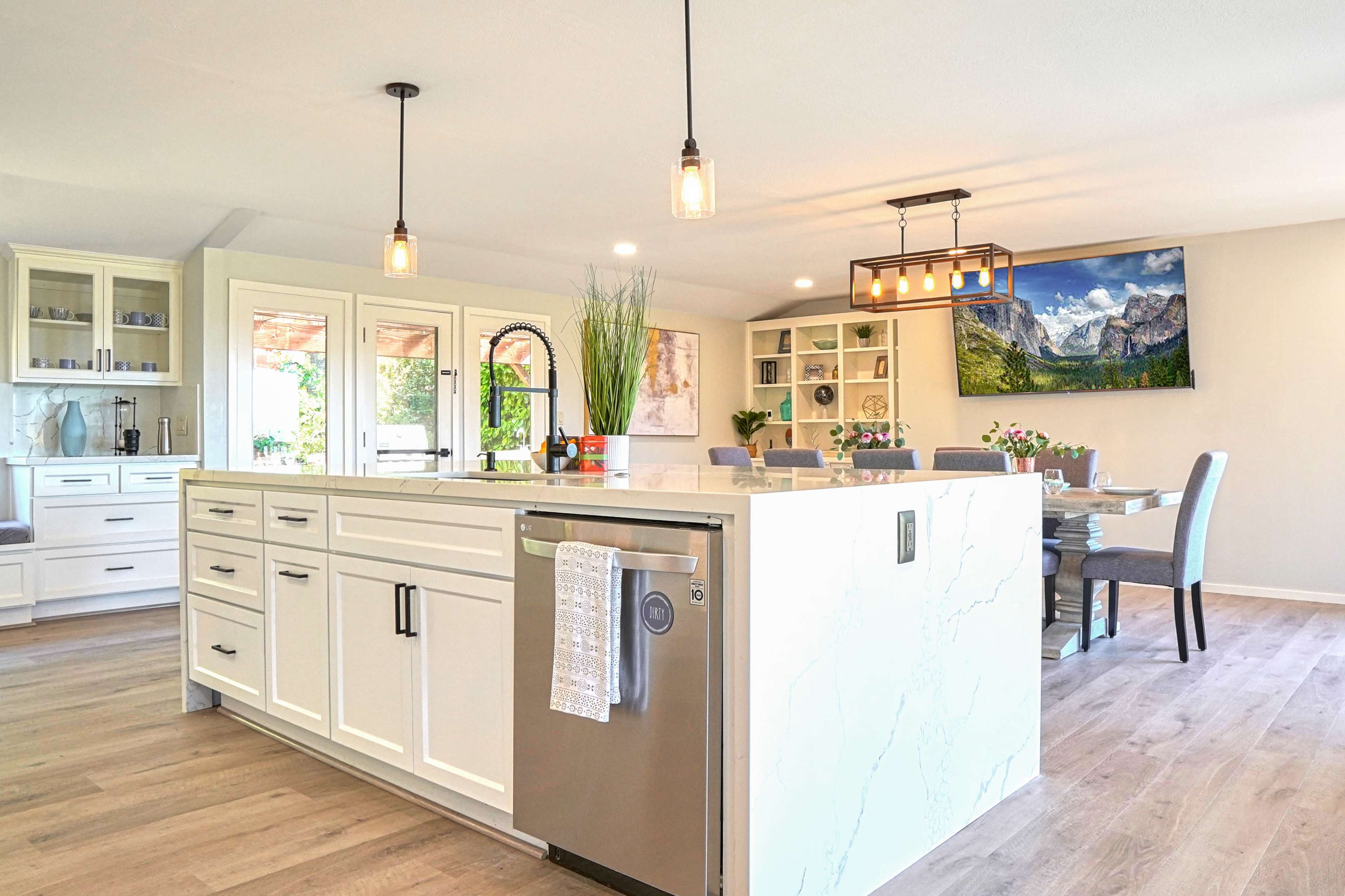 A bright and modern kitchen features white cabinetry, a large island, and an adjoining dining area with a mountain landscape on the wall.