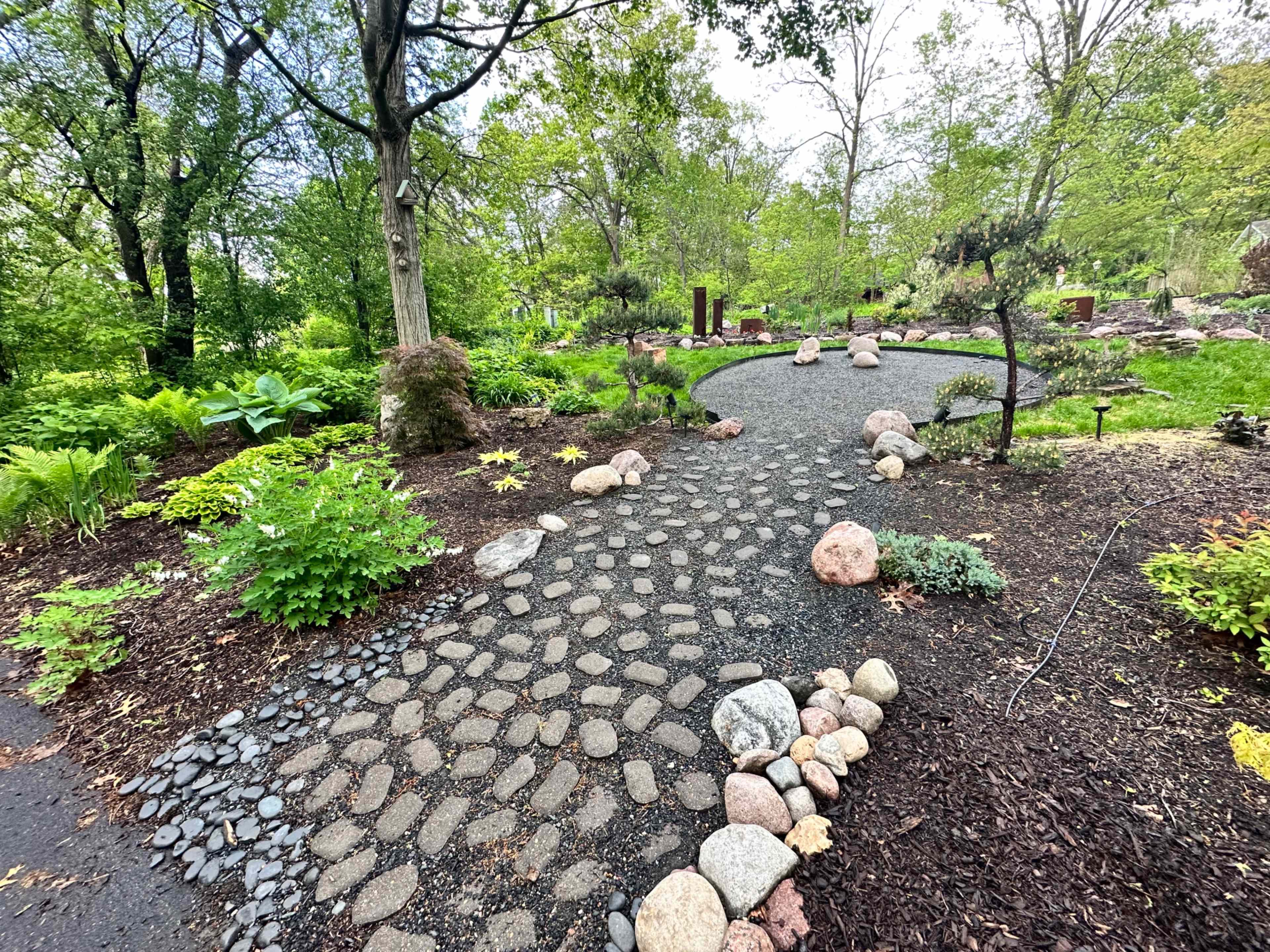 A winding pebble pathway bordered by assorted rocks and plants leads through a landscaped garden.