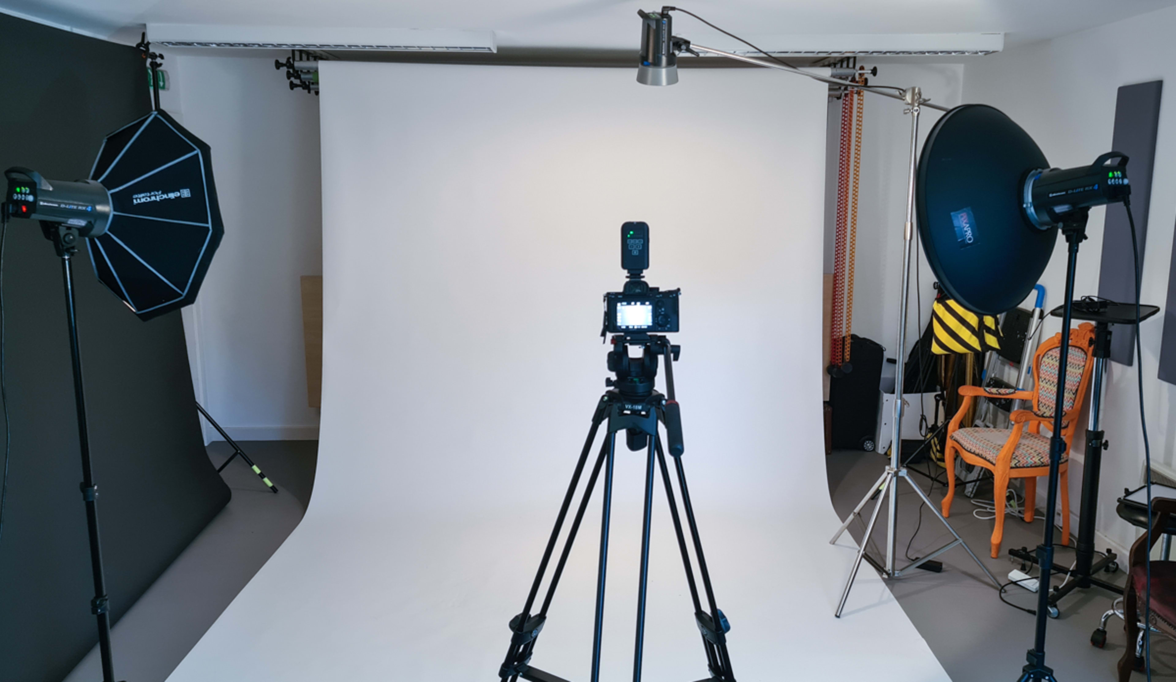 A photography studio setup with a camera on a tripod facing a plain backdrop illuminated by softbox lights.