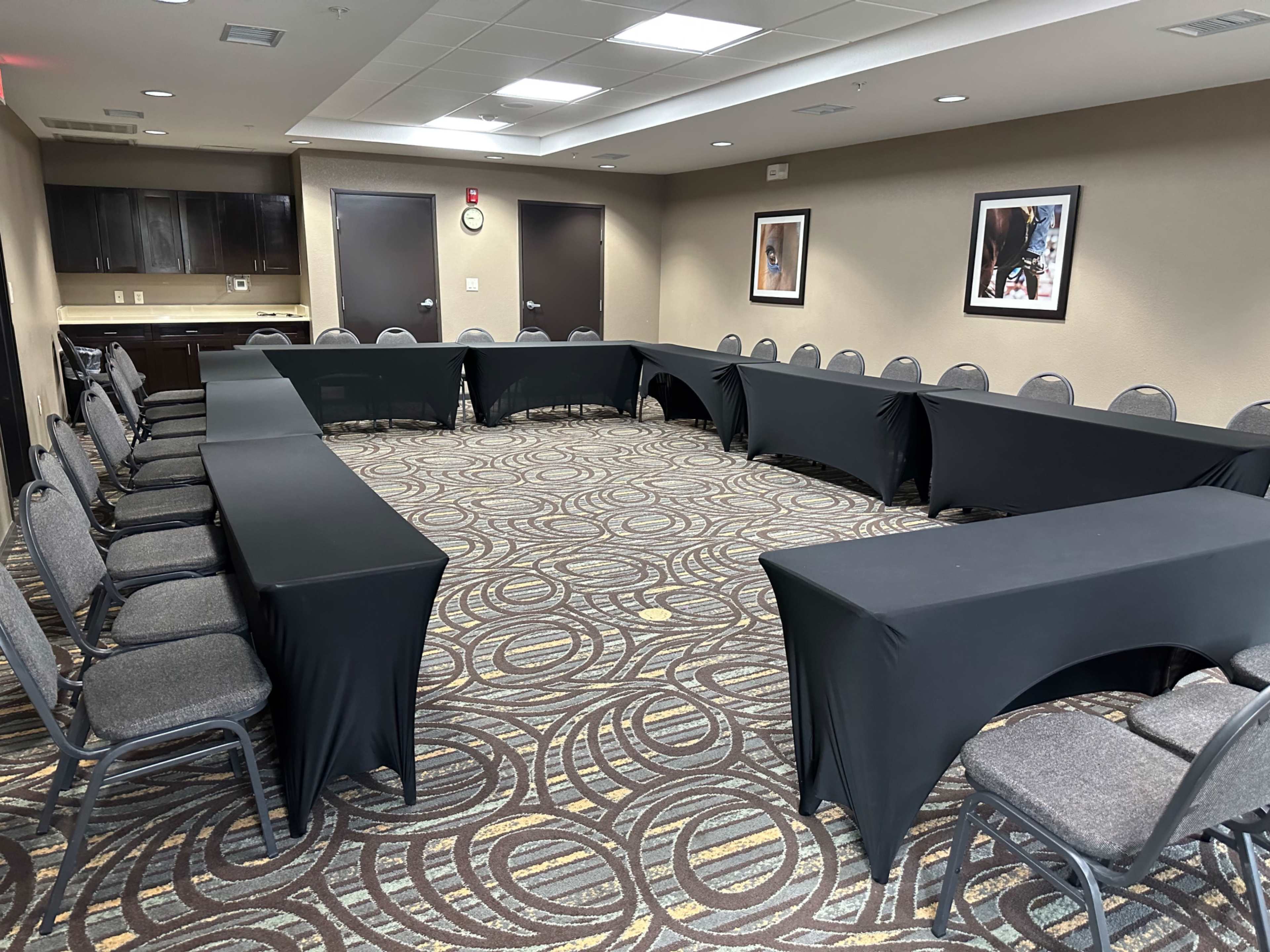 A conference room set up with a large U-shaped arrangement of tables covered in black cloth, surrounded by gray chairs.