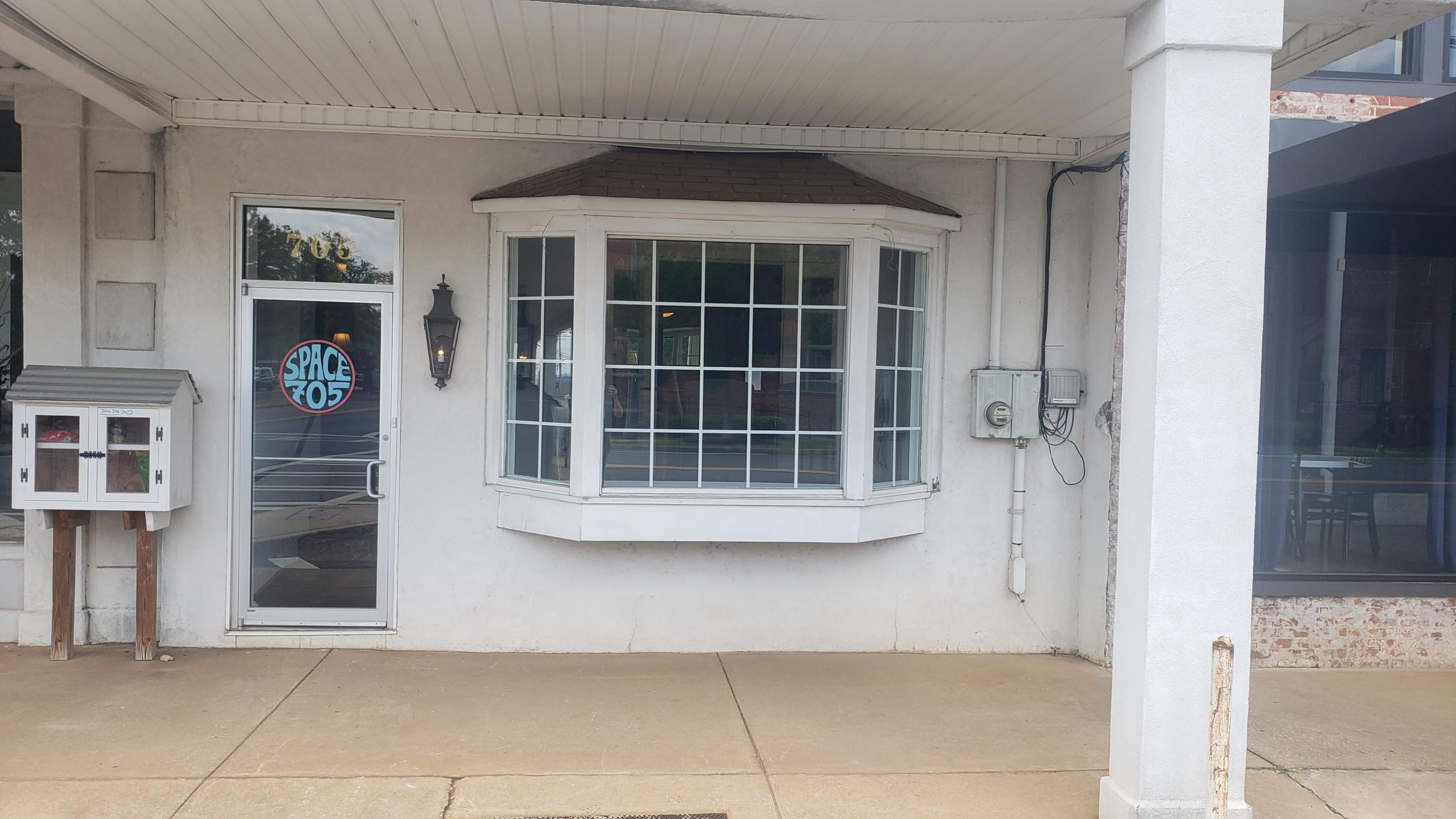 A building exterior featuring a large bay window and a door with a circular sign labeled "SPACE 705."