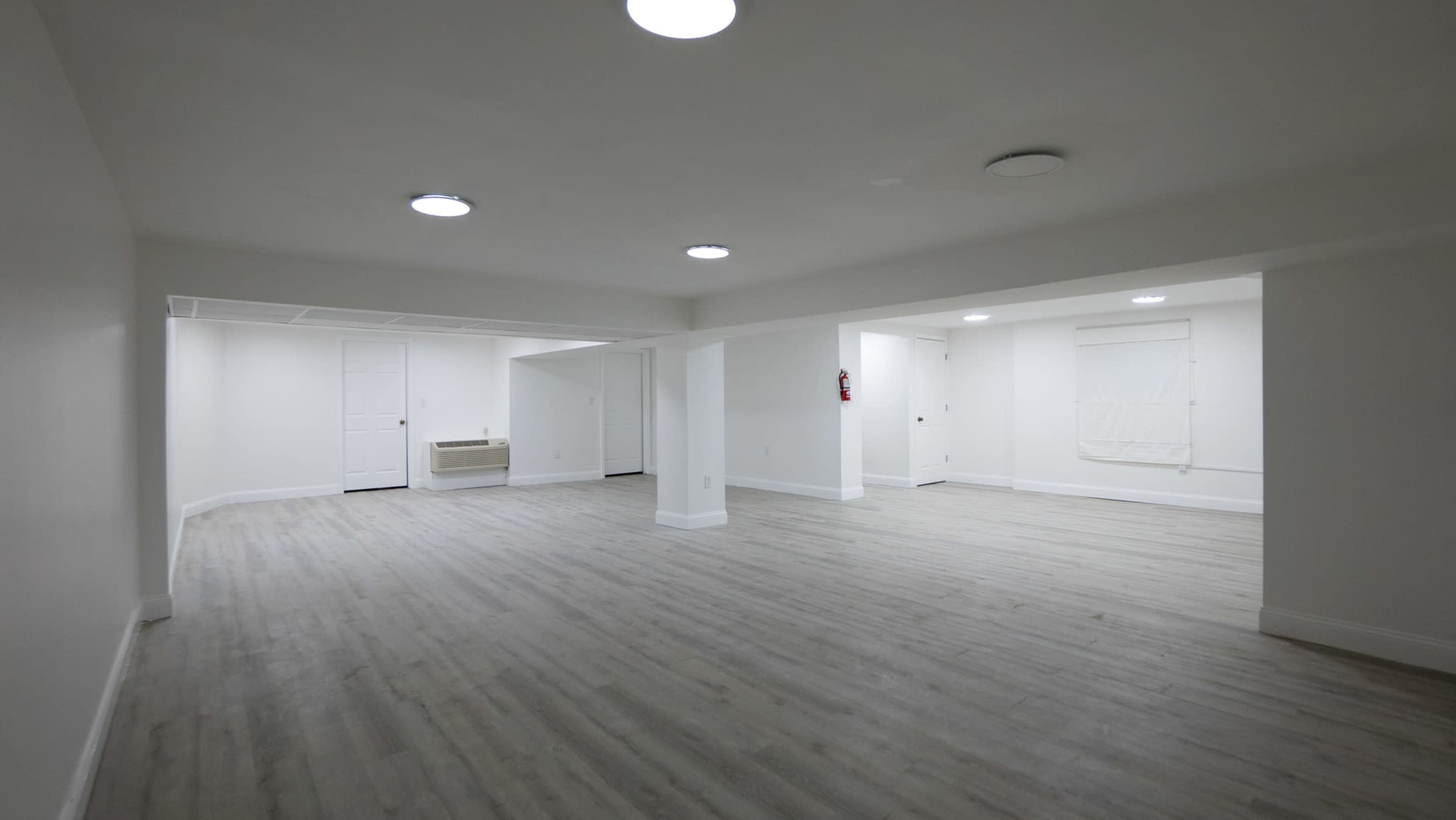 A spacious, unfinished basement with light-colored walls and a light wooden floor, featuring multiple ceiling lights.