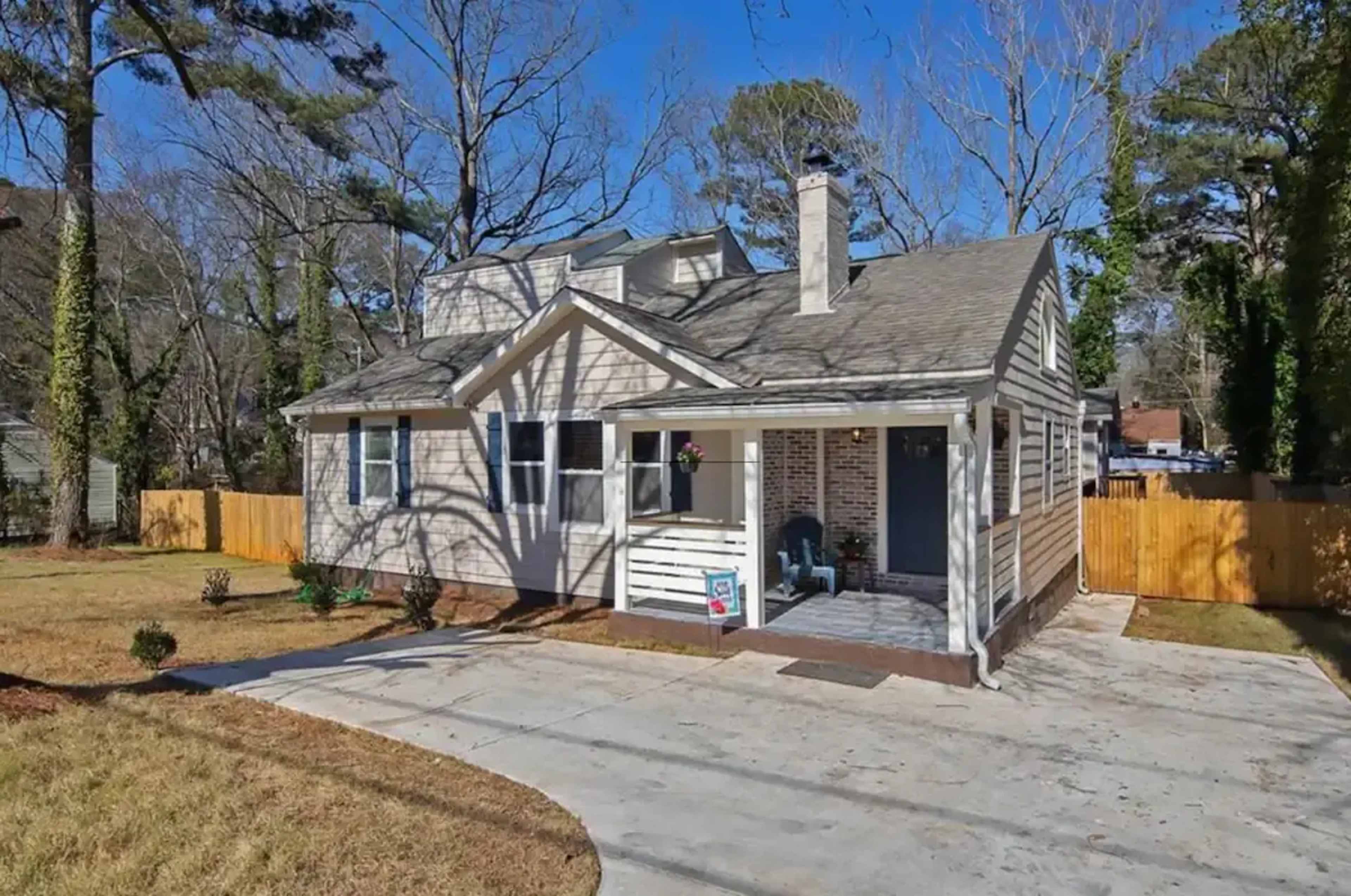 A single-story house with a front porch and a driveway is set against a clear blue sky.
