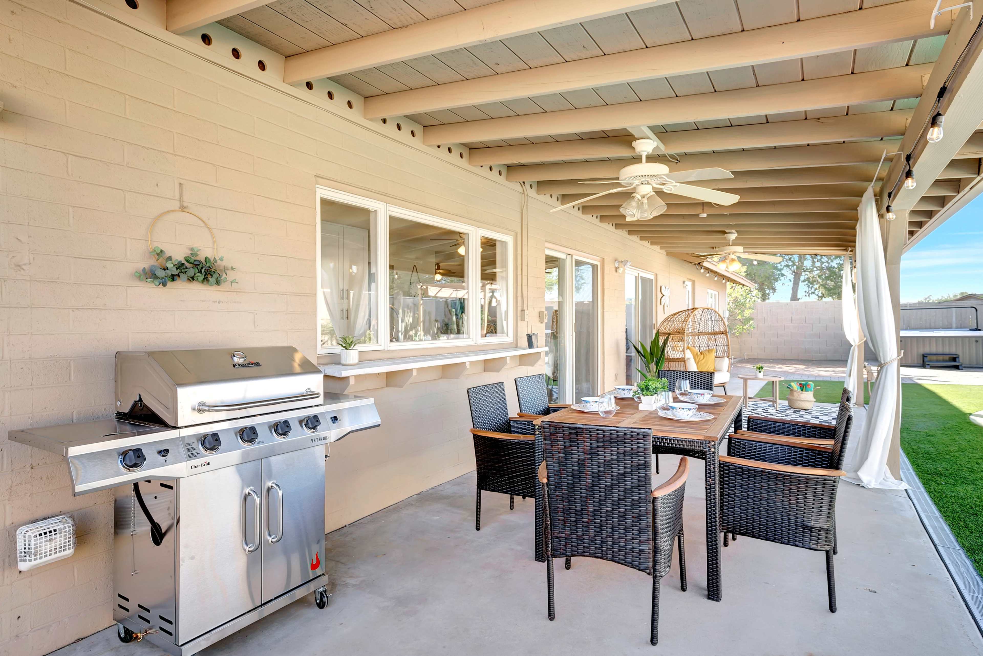 A covered patio with a dining table set for six, a barbecue grill, and a small green lawn visible in the background.