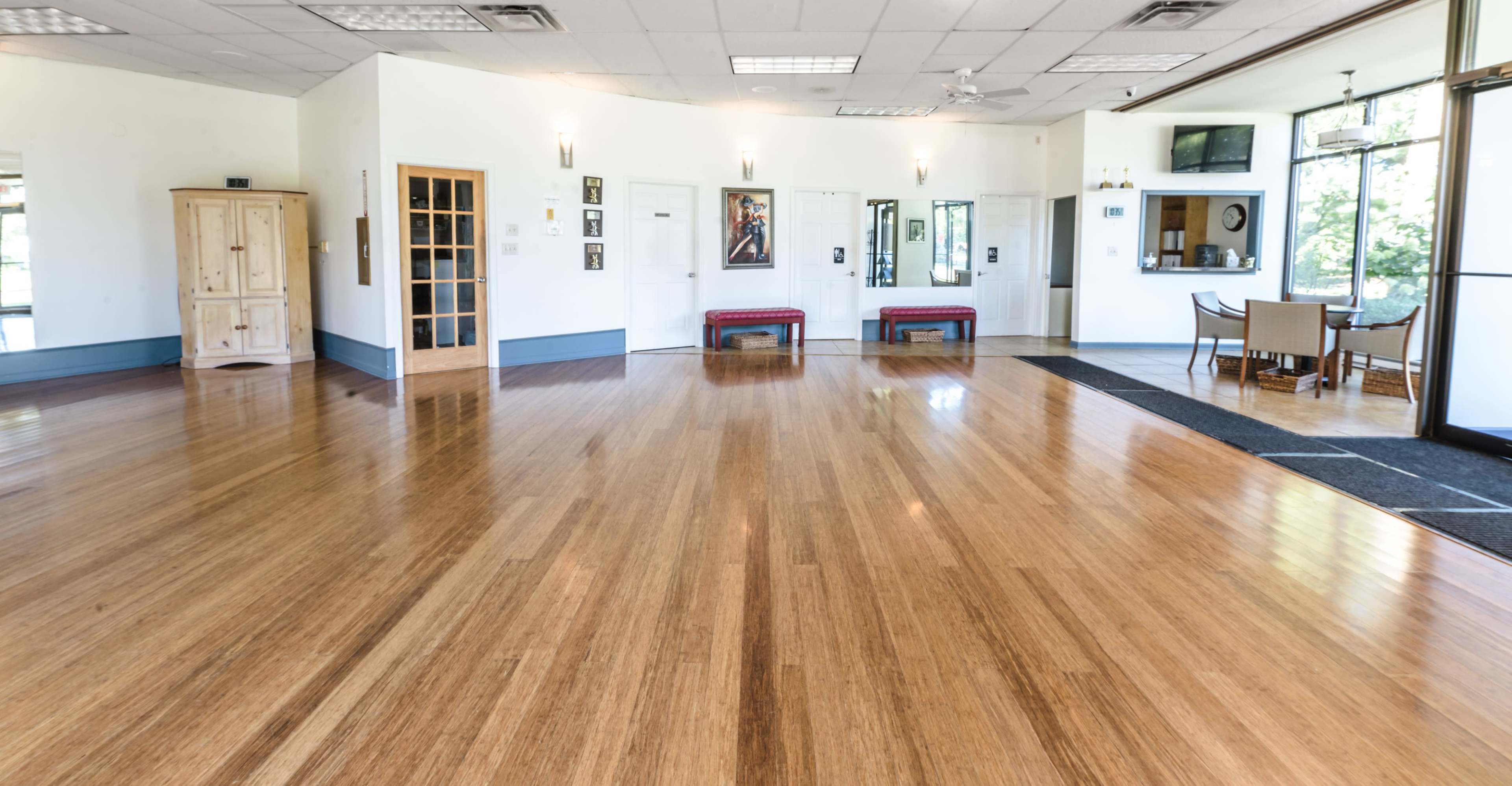 A spacious interior room with polished bamboo flooring, mirrored walls, and a seating area with benches and a dining space in the background.