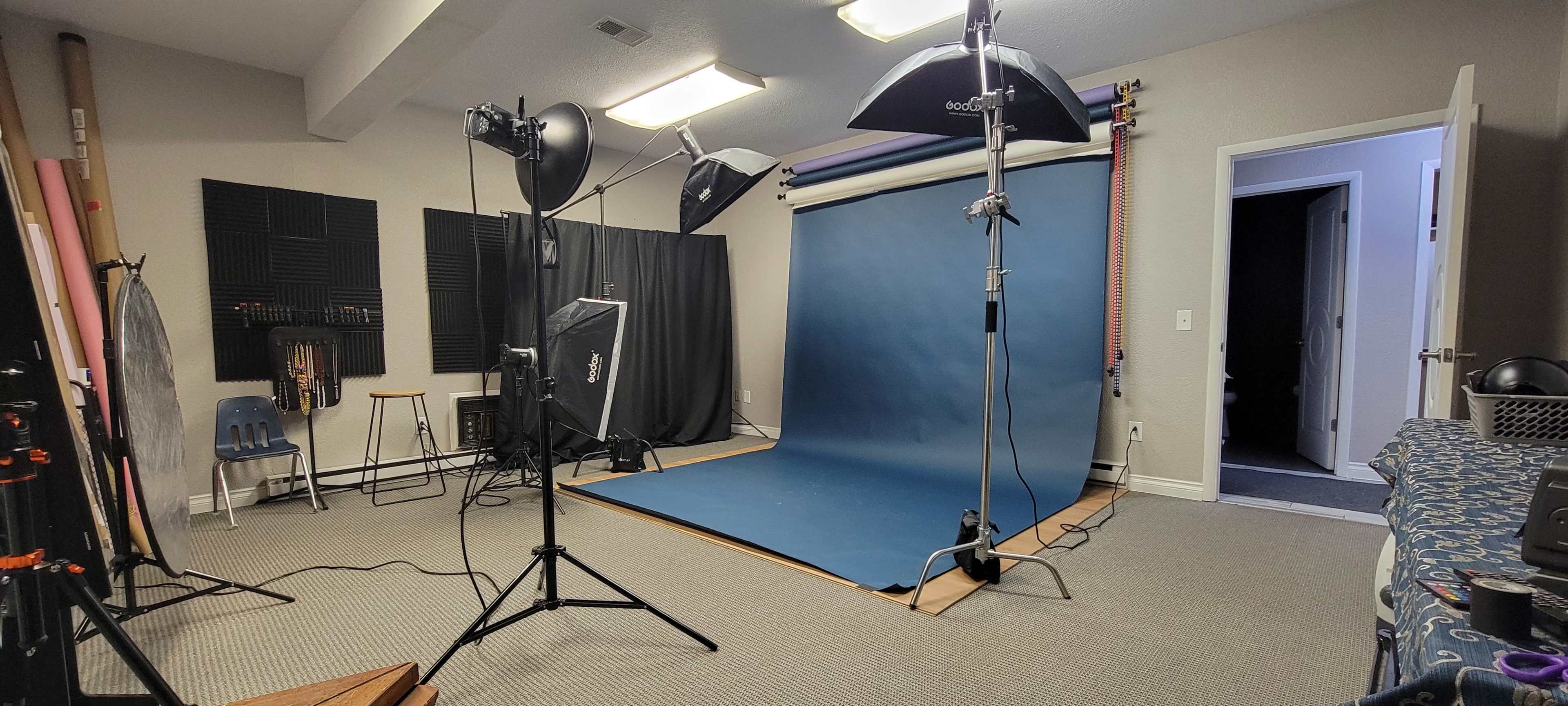 A photography studio with a blue backdrop, various lighting equipment, and a chair in the corner.