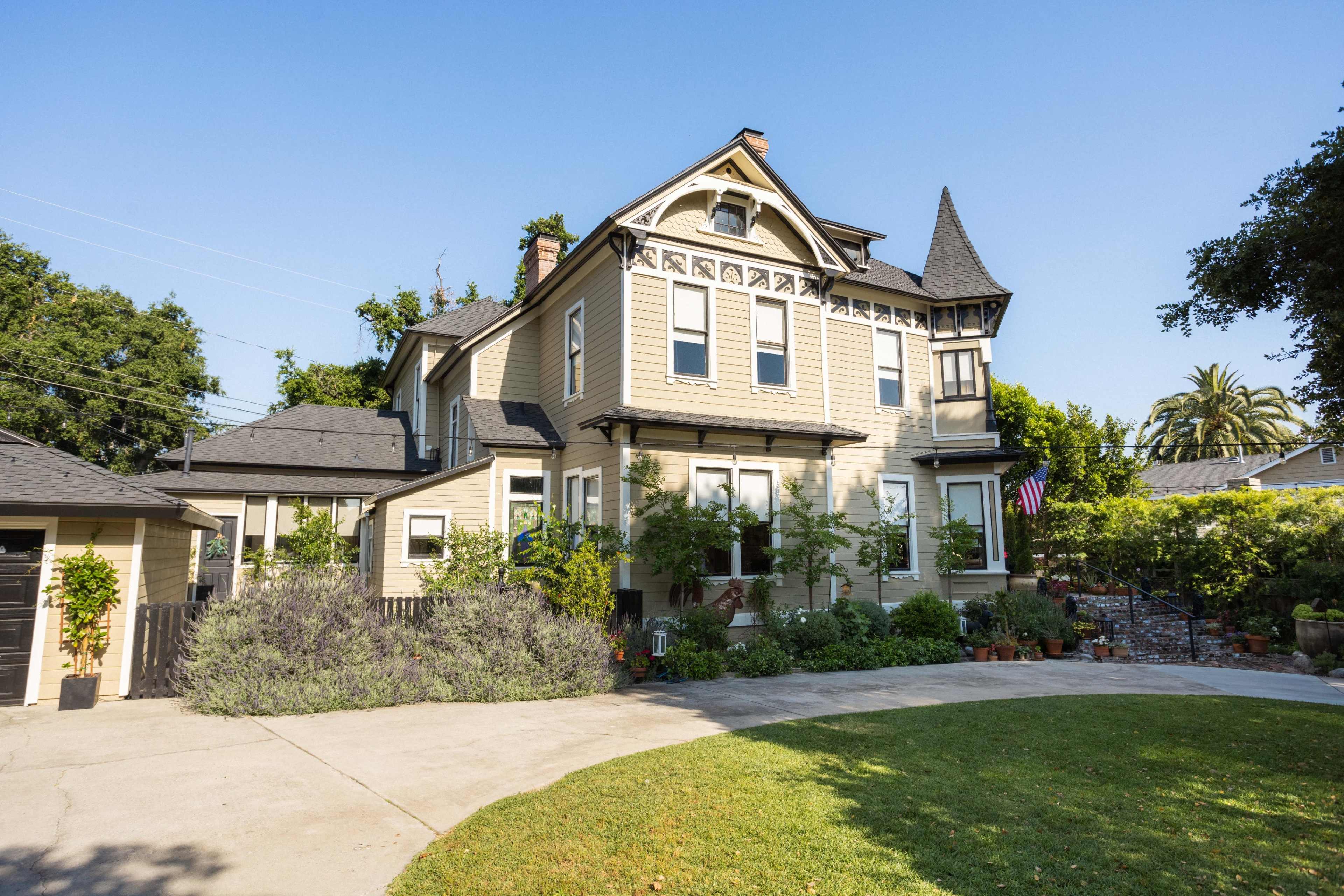 A large Victorian-style house with a pointed rooftop and a circular driveway surrounded by landscaped greenery.