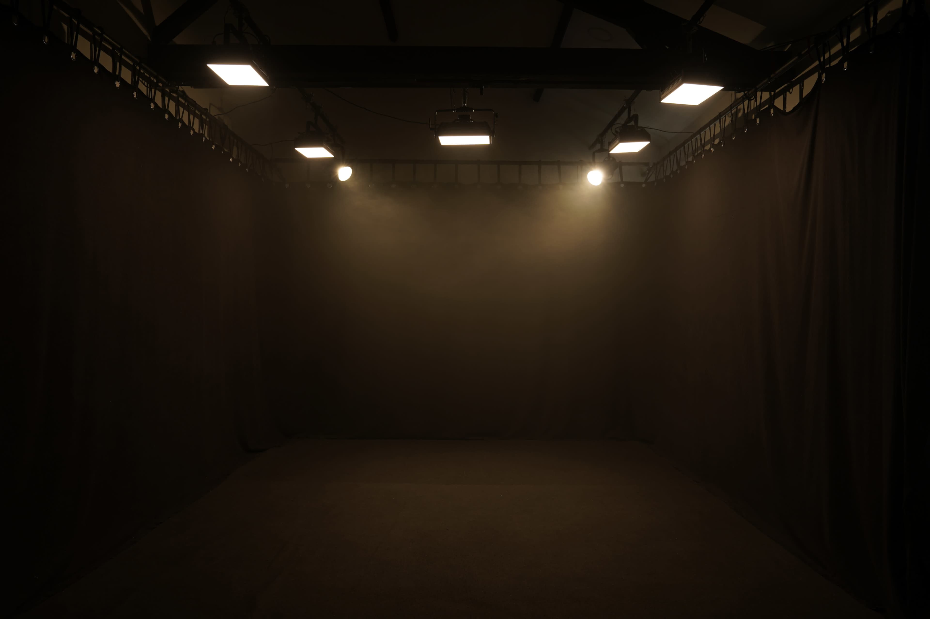 An empty room with dark walls and ceiling, illuminated by overhead lights creating a focused glow in the center.