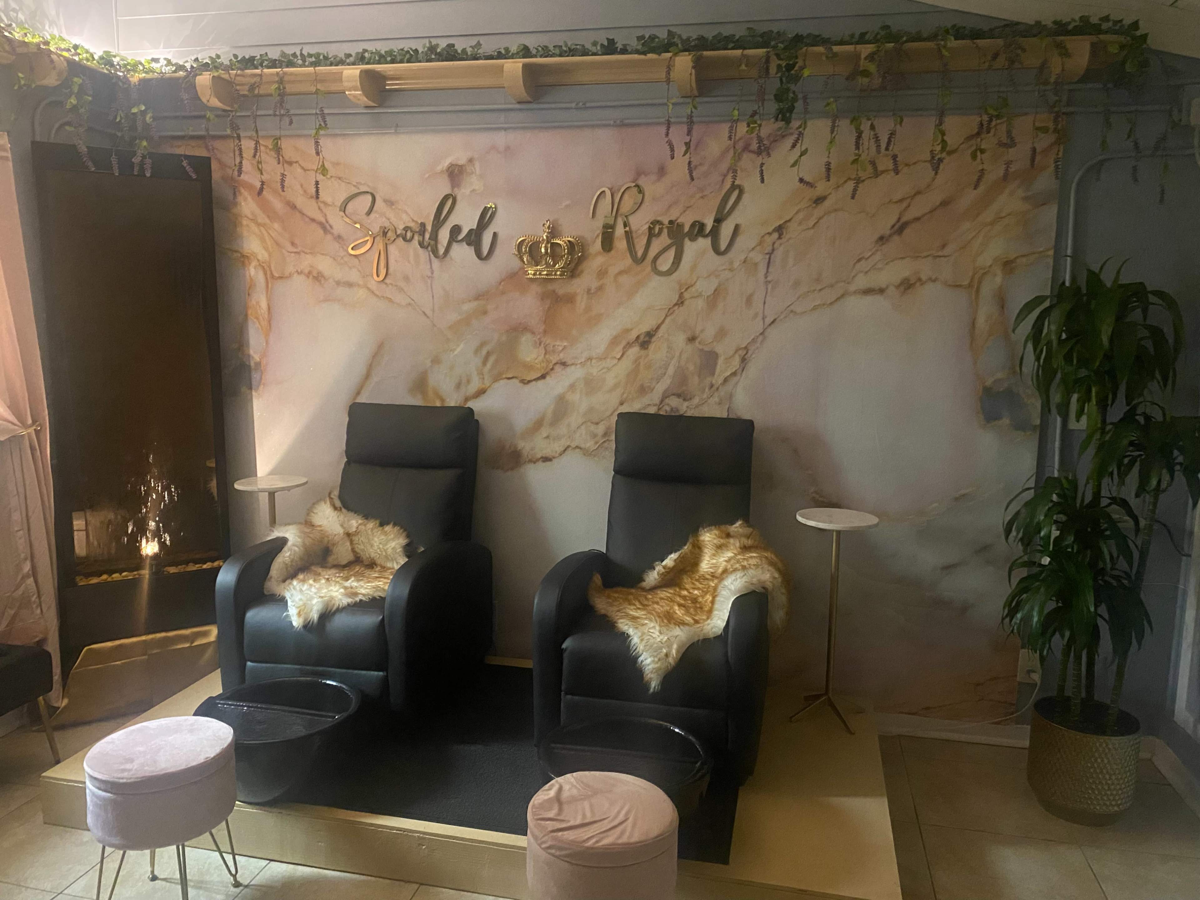 A serene spa-like interior with two black reclining chairs, a marble-patterned wall, and decorative elements including a crown sign and plants.