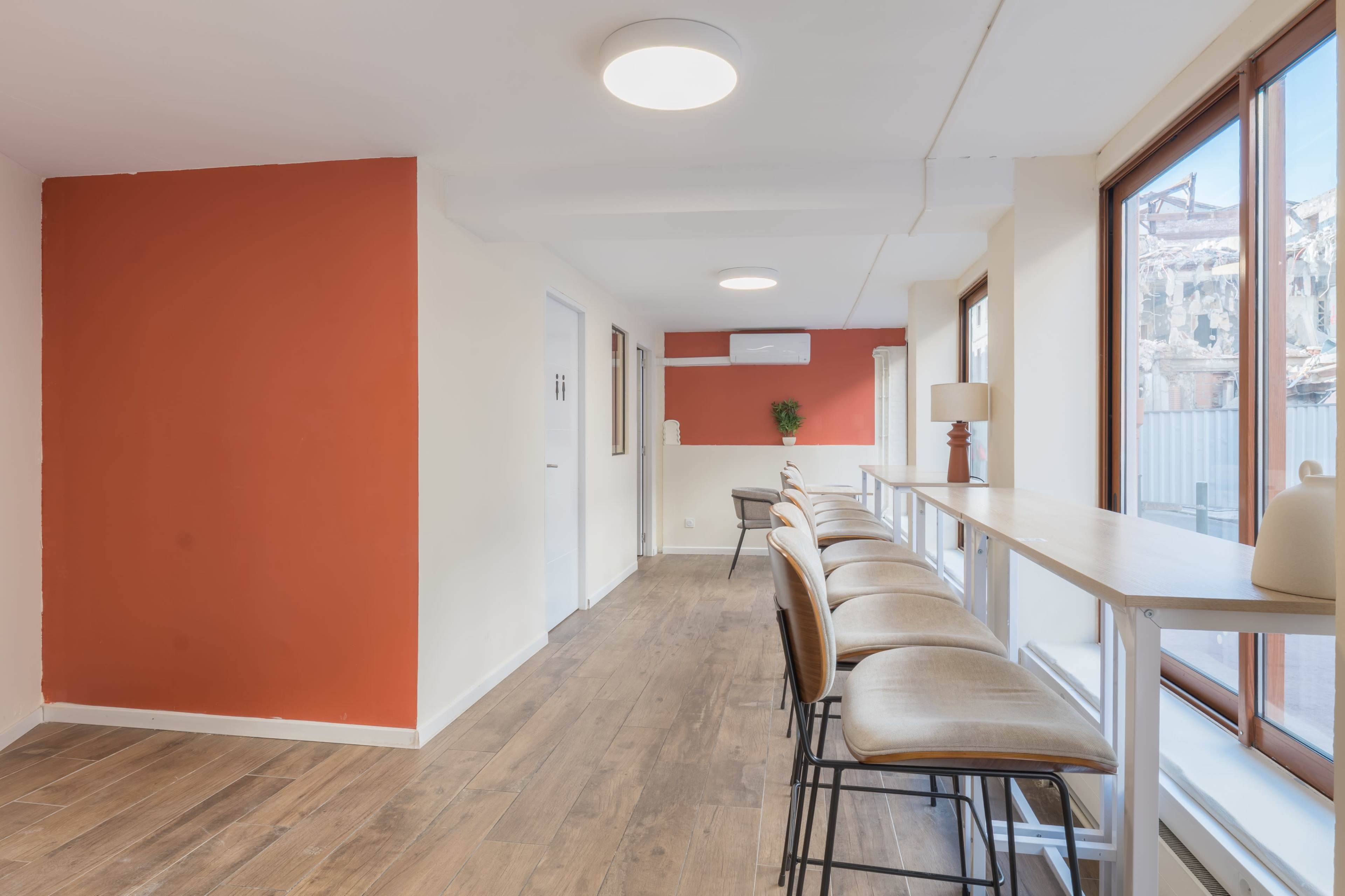 The image shows a modern interior space with a row of high stools at a counter, white walls, and an accent wall painted orange.