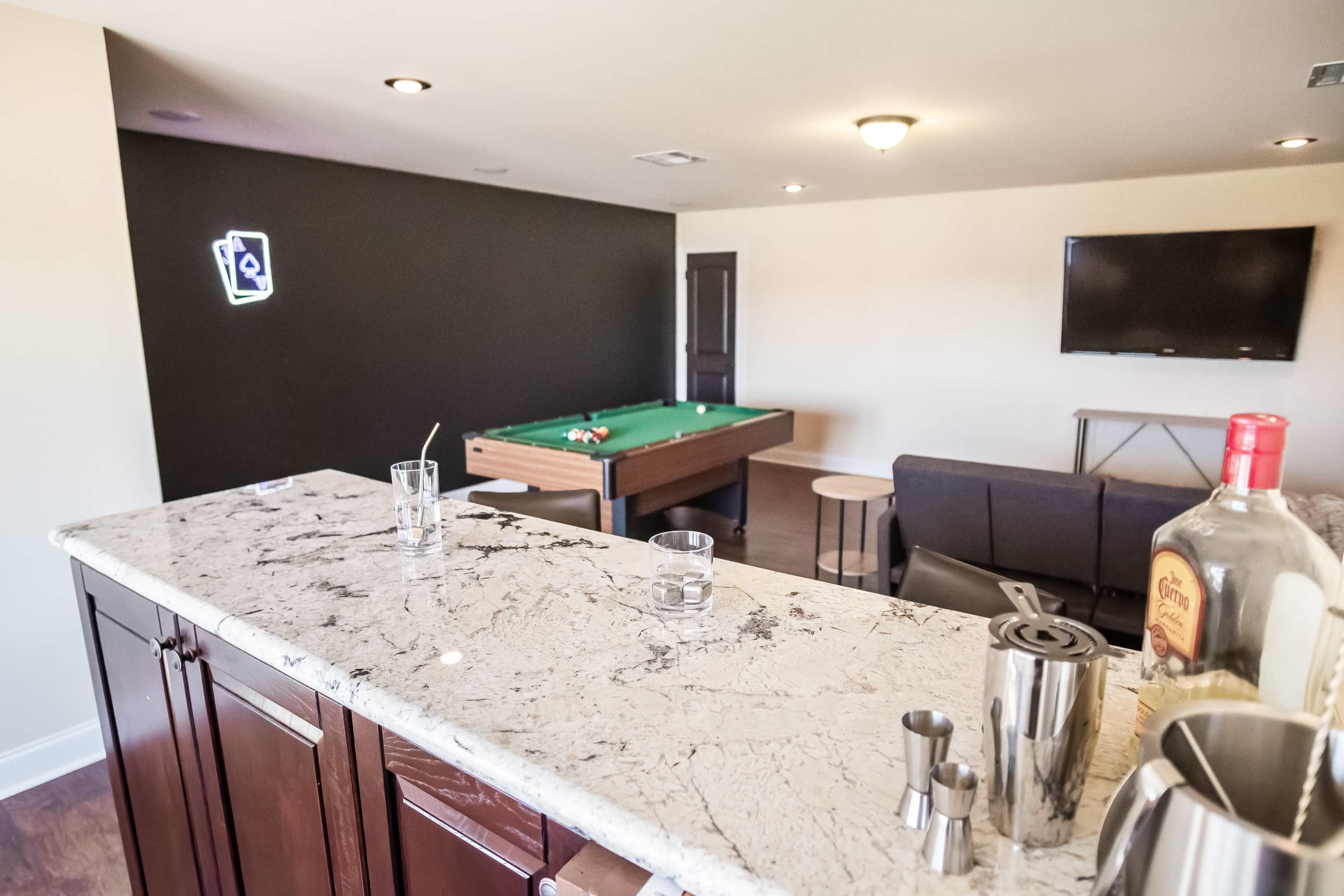 A modern game room with a pool table, a bar counter, and a television mounted on the wall.
