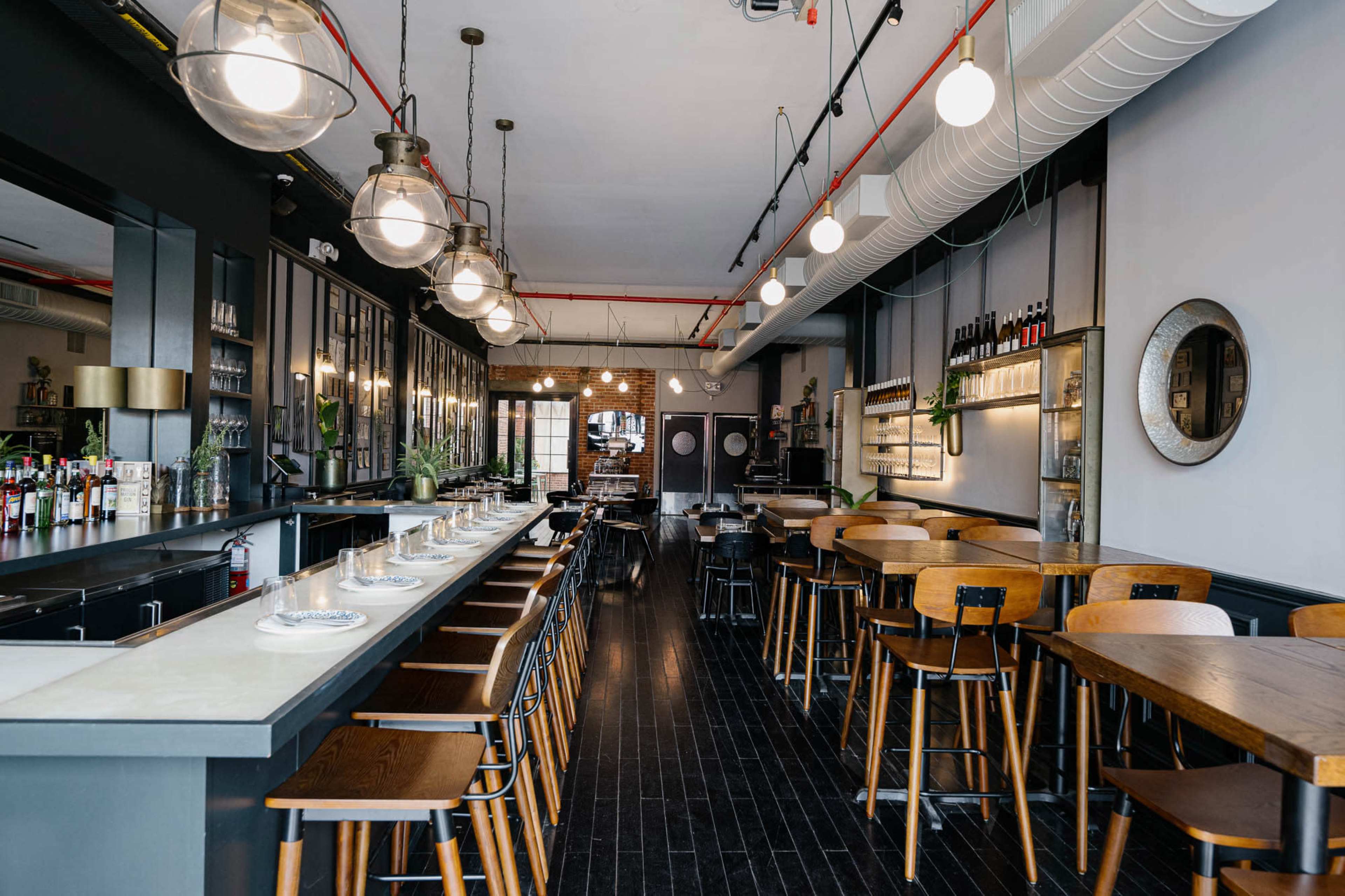 The image shows a modern restaurant interior with a long bar, wooden tables, and various light fixtures illuminating the space.