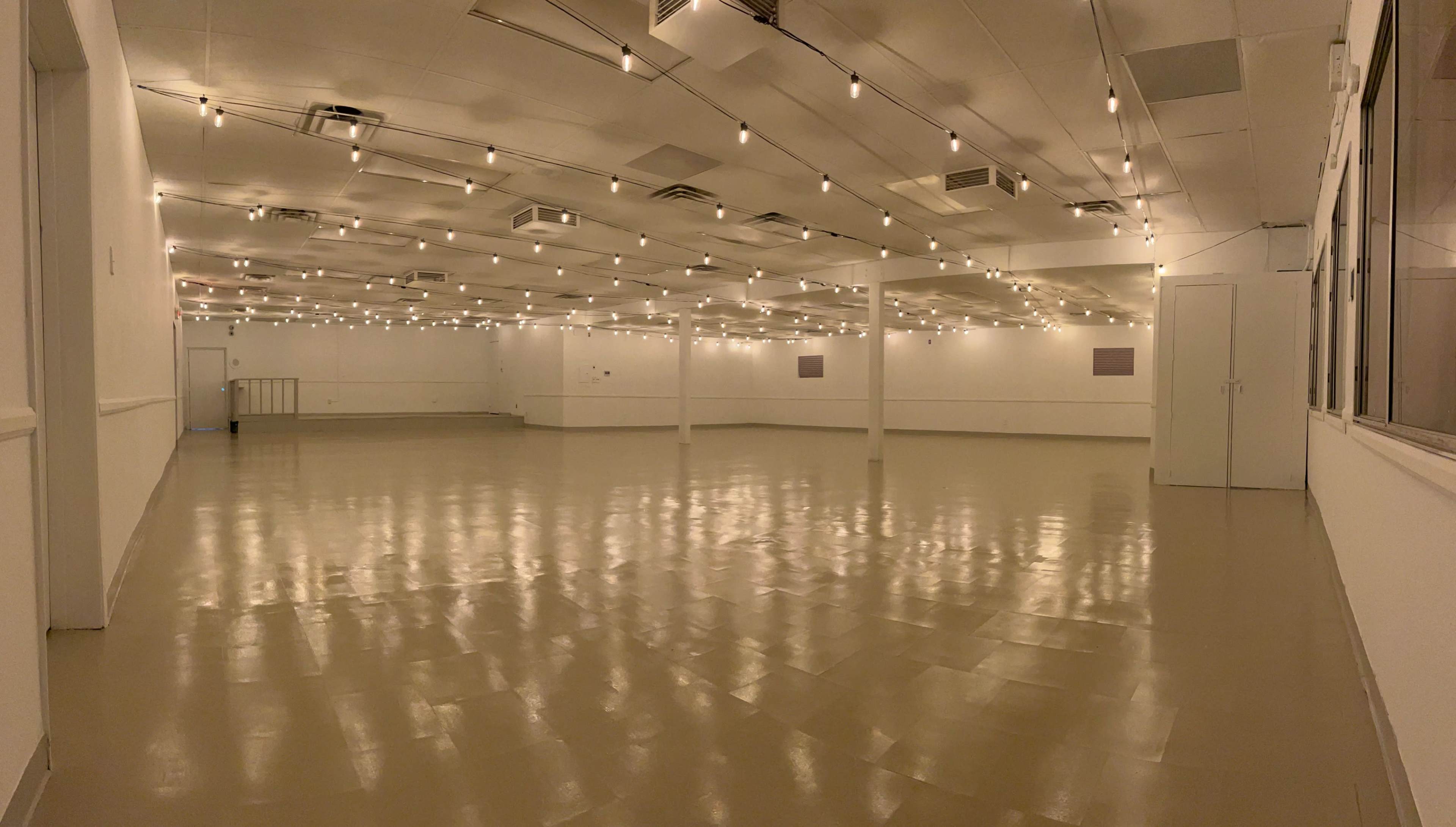 A spacious, empty room with polished floors and dim, string lights hanging from the ceiling.