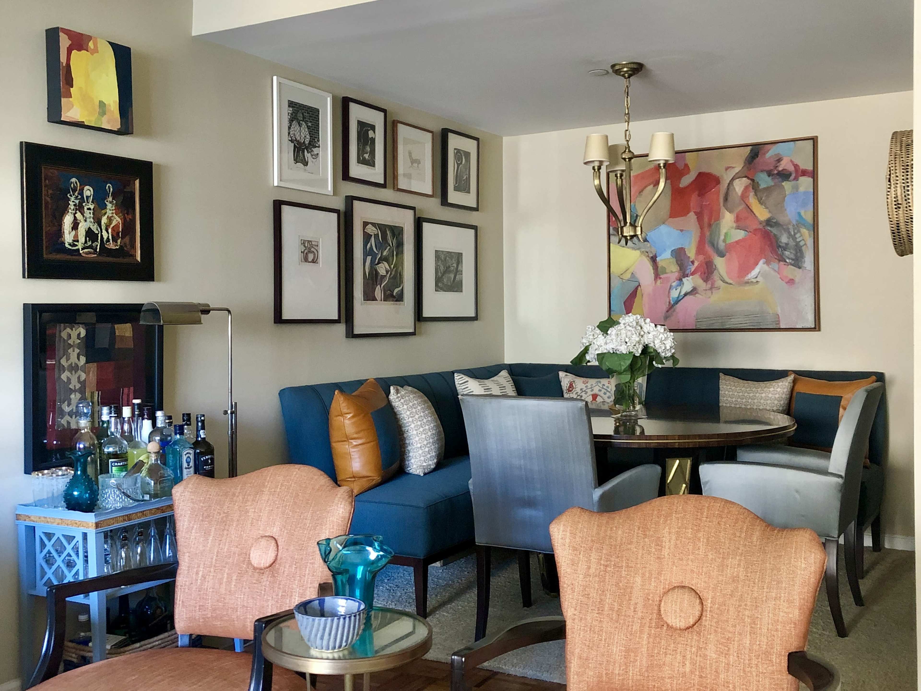 A modern living area featuring a blue sectional sofa, a round dining table surrounded by chairs, and various framed artworks on the walls.
