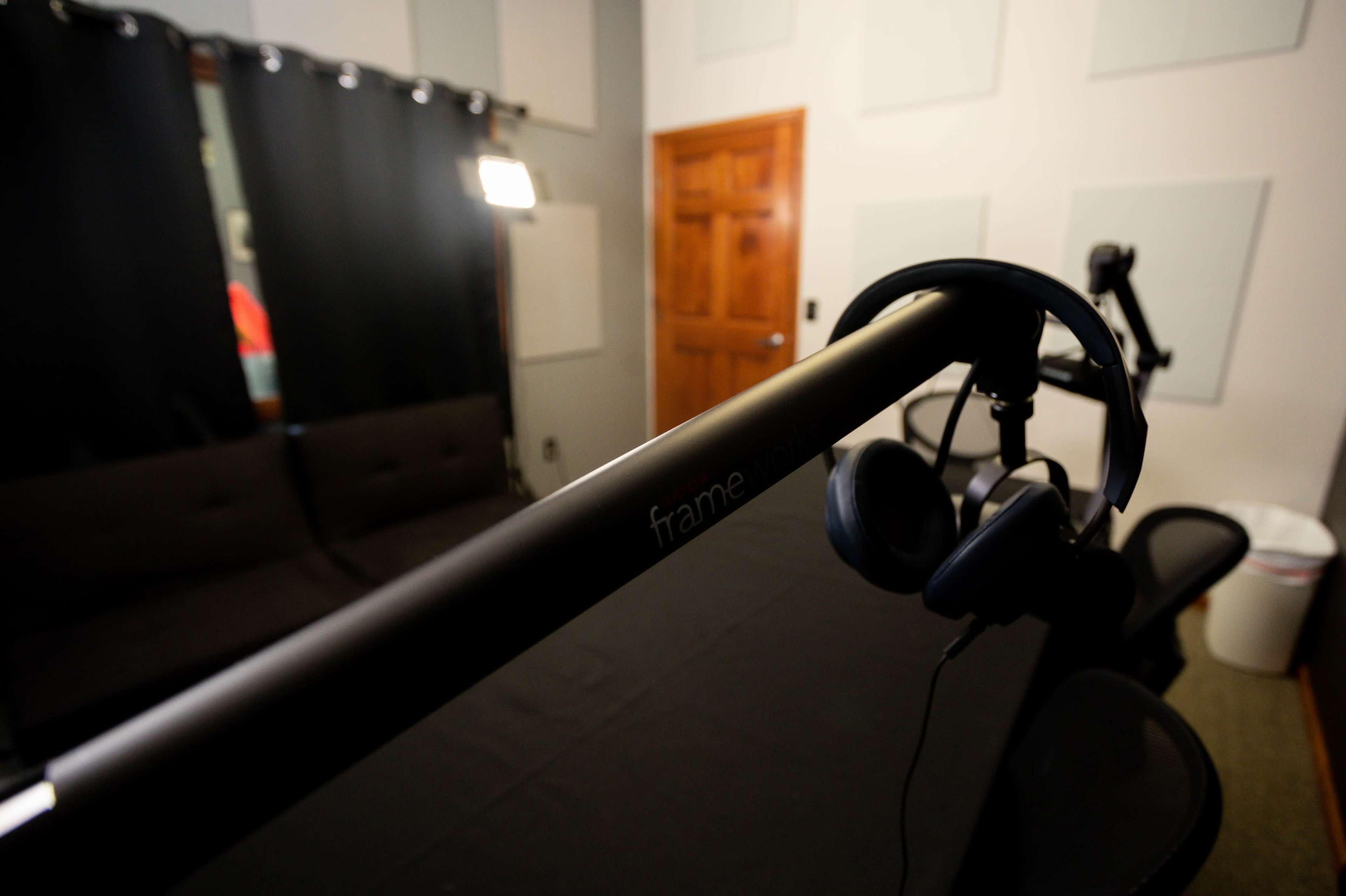 A microphone stand with headphones hangs over a black table in a soundproof room featuring a couch and curtains.