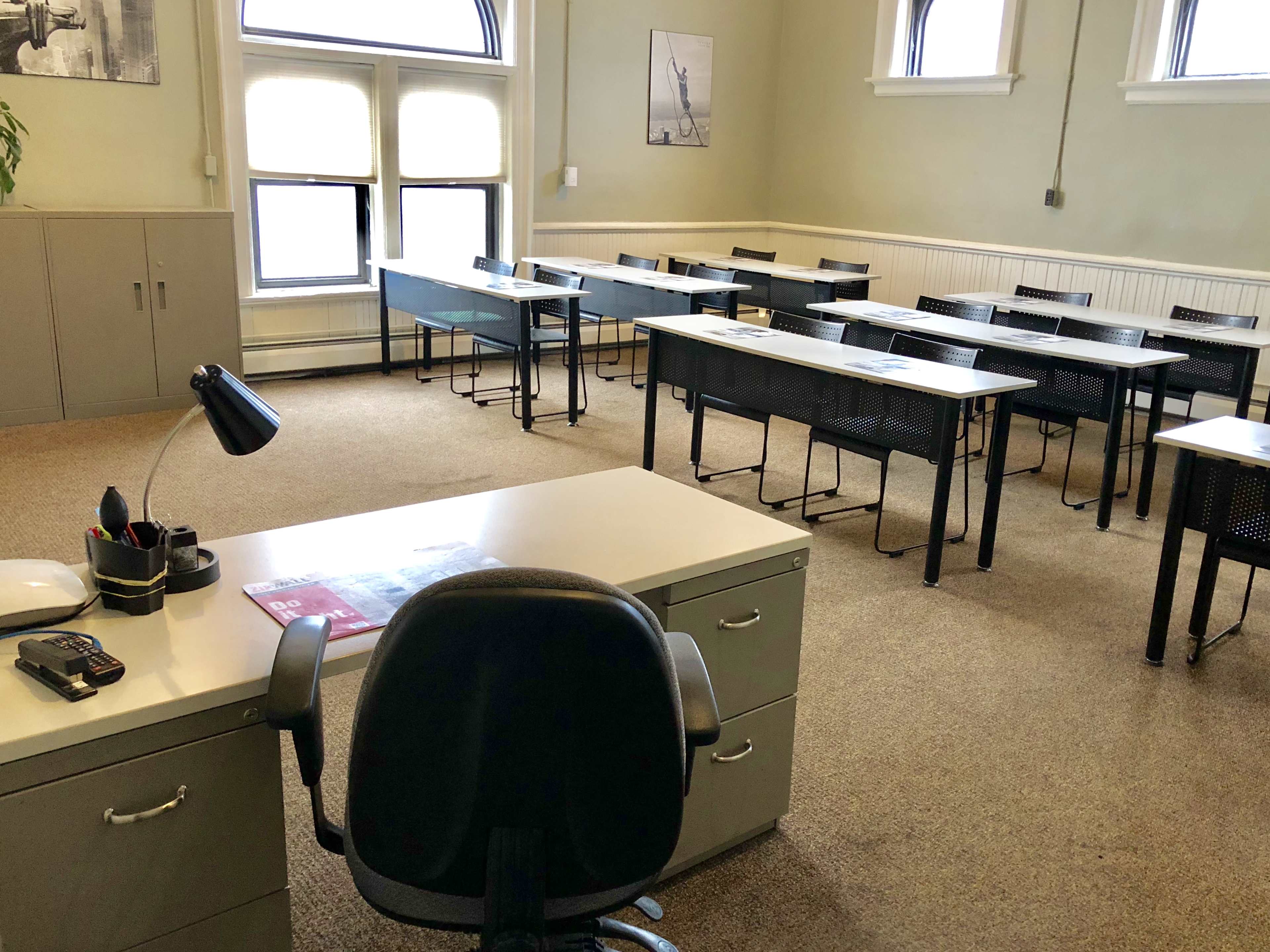 A classroom with several rows of desks and a teacher's desk situated at the front.
