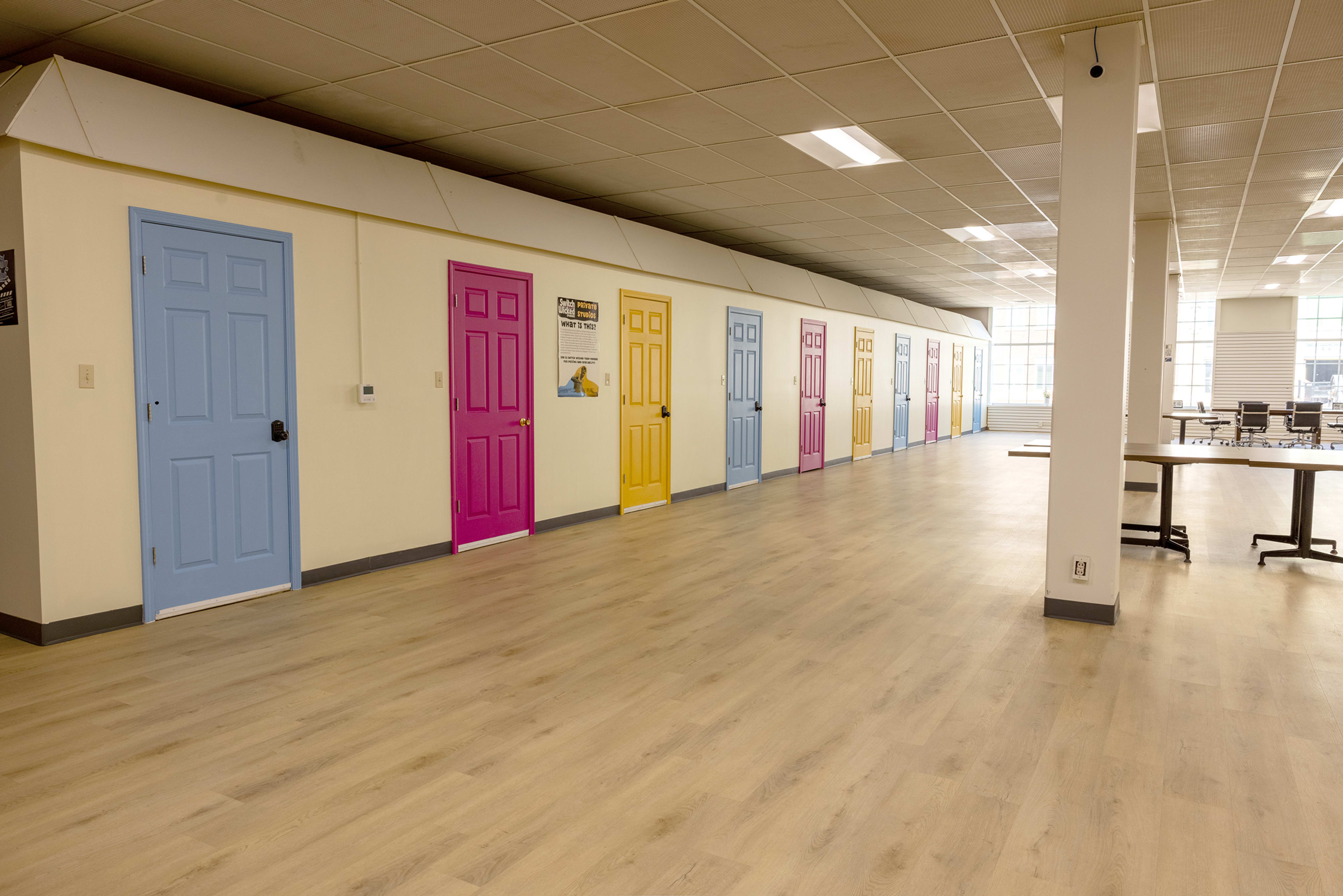 The image shows a long hallway with a series of brightly colored doors in shades of blue, pink, yellow, and purple along one wall.