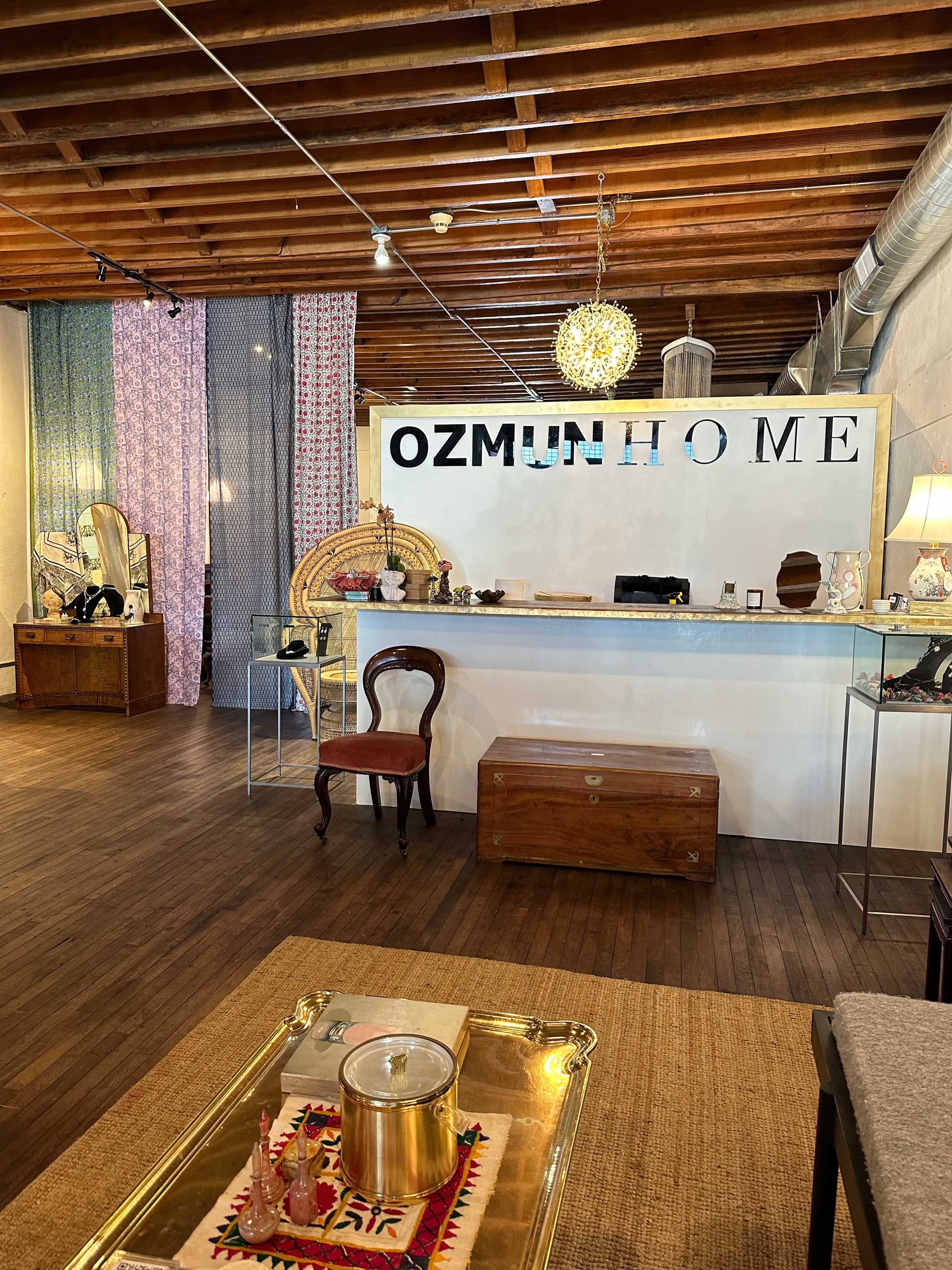 An interior of a home goods store featuring wooden furniture, decorative items, and a display area with the name "OZMUH HOME" prominently displayed on the wall.