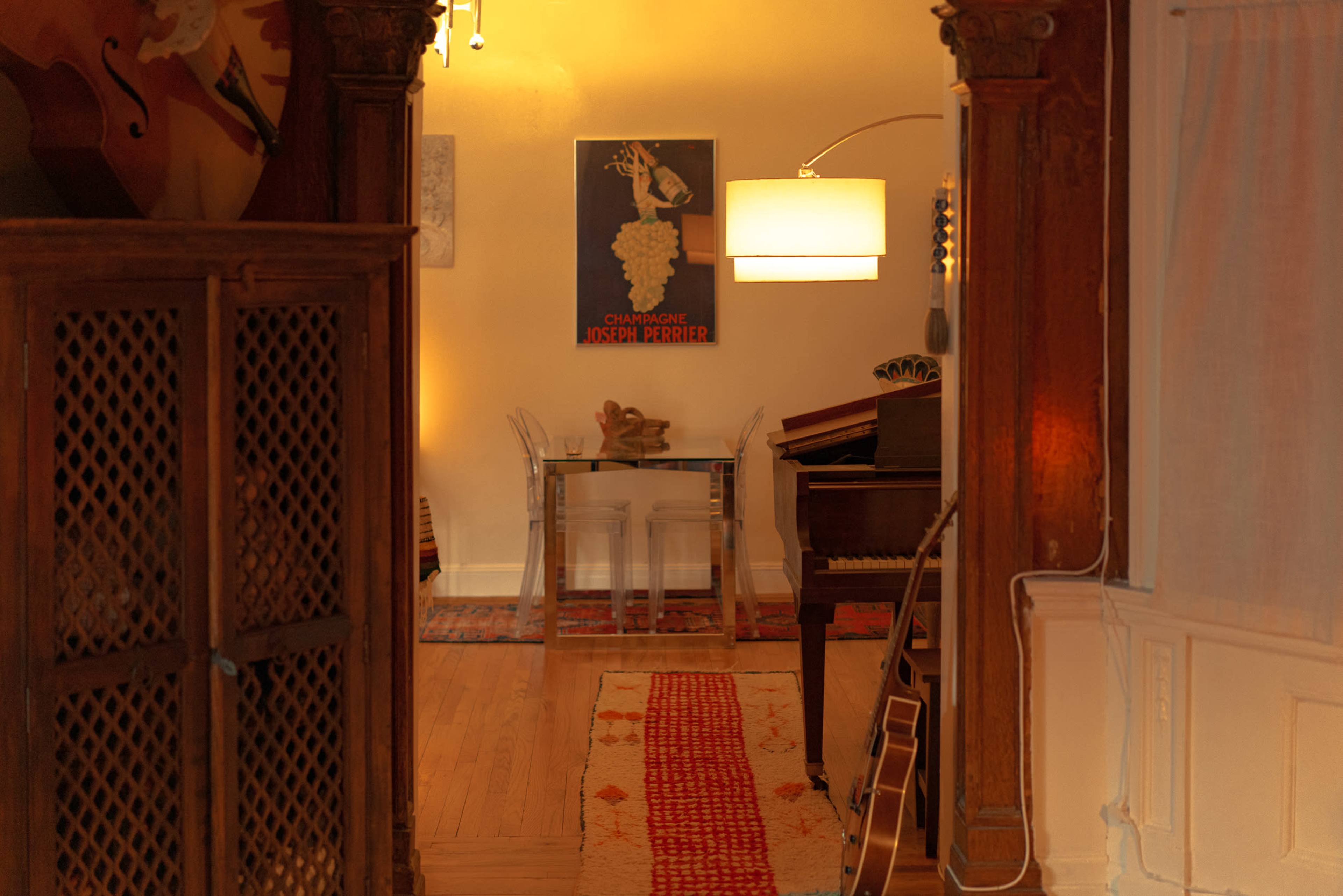 A narrow hallway leads to a small room featuring a piano, a clear table, and a poster on the wall.