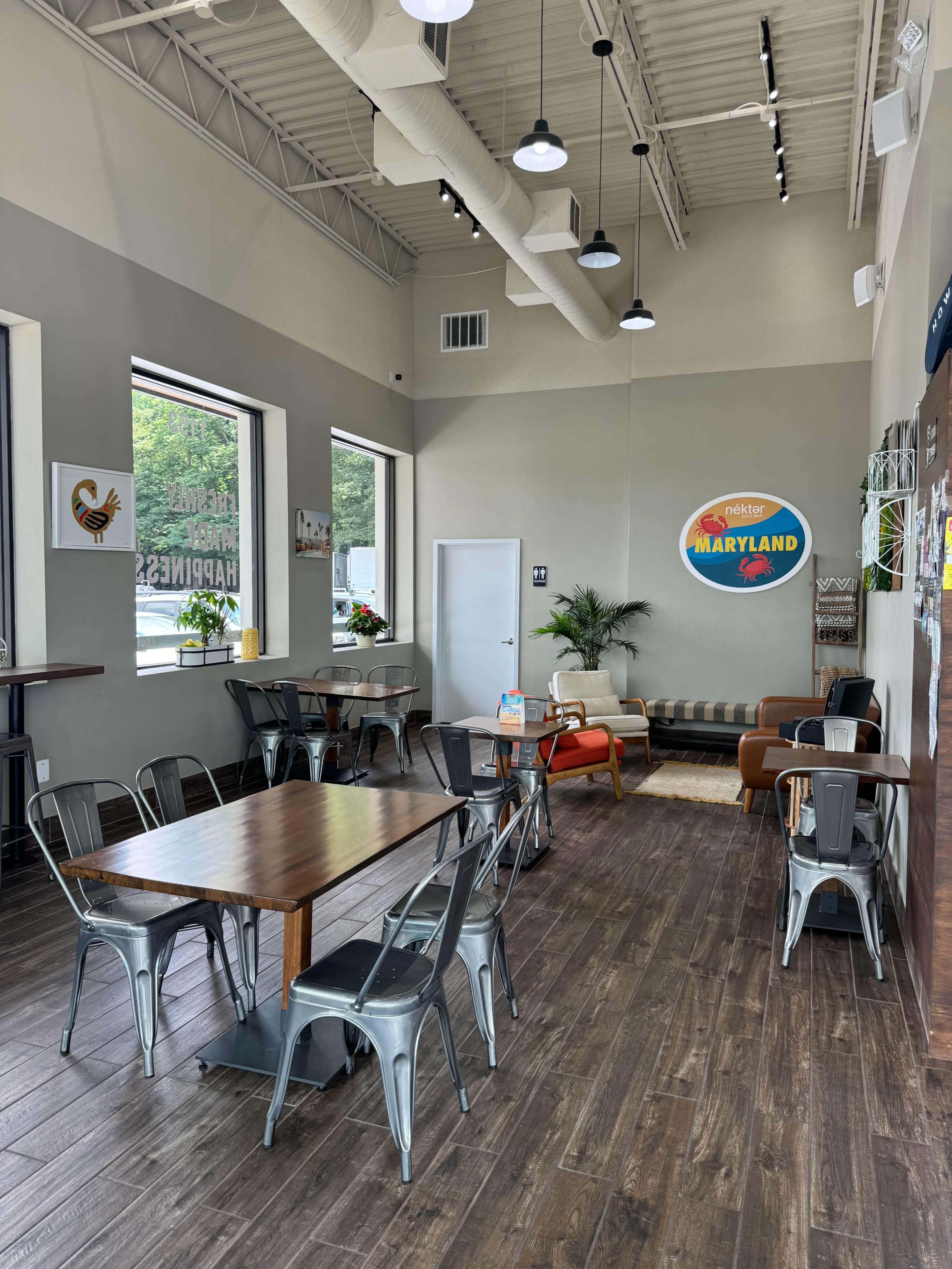 A spacious, modern café with seating options including metal chairs and wooden tables, along with a sofa and decorative wall art.