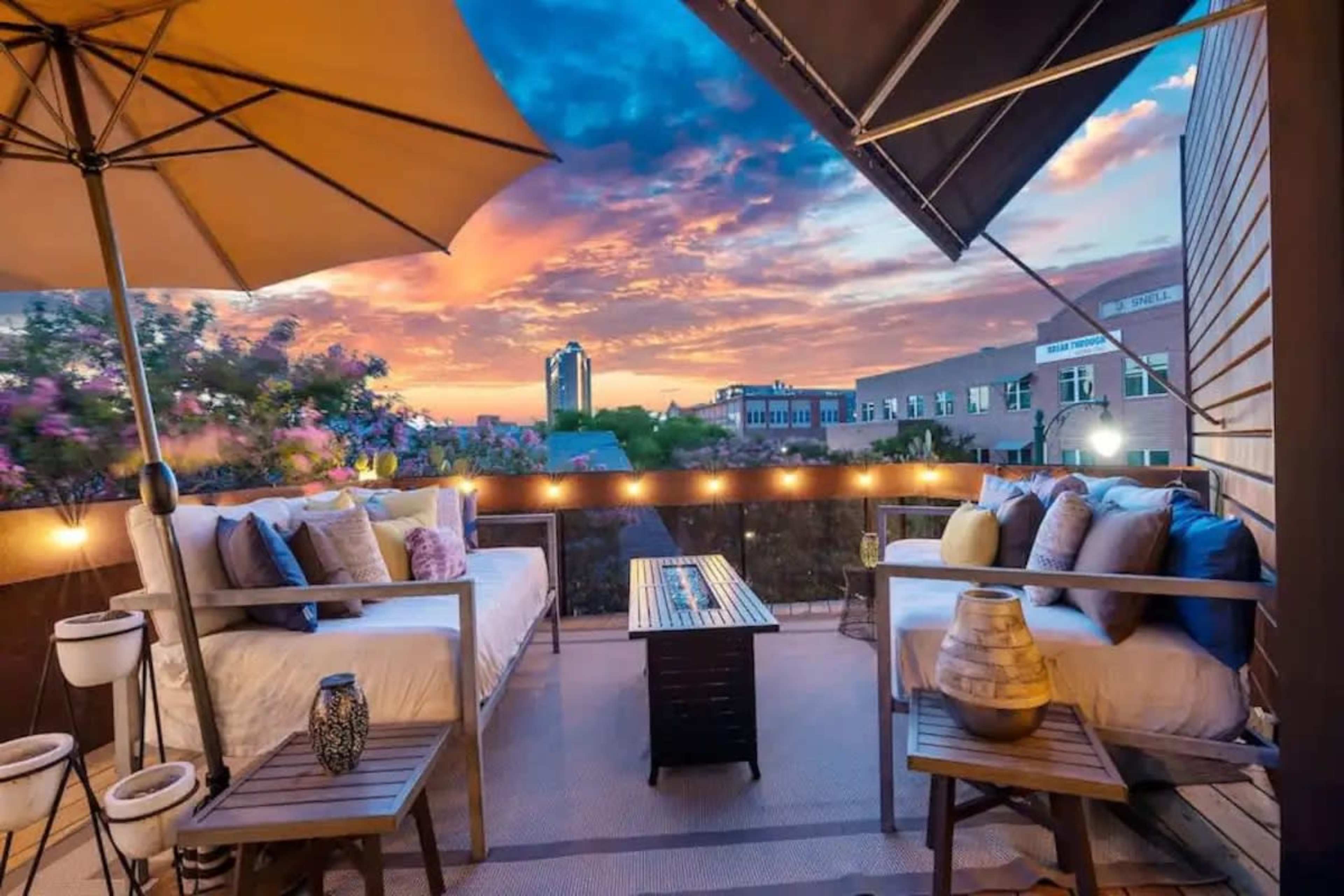 A rooftop patio features two sofas, a coffee table, and decorative items, with a sunset sky in the background.