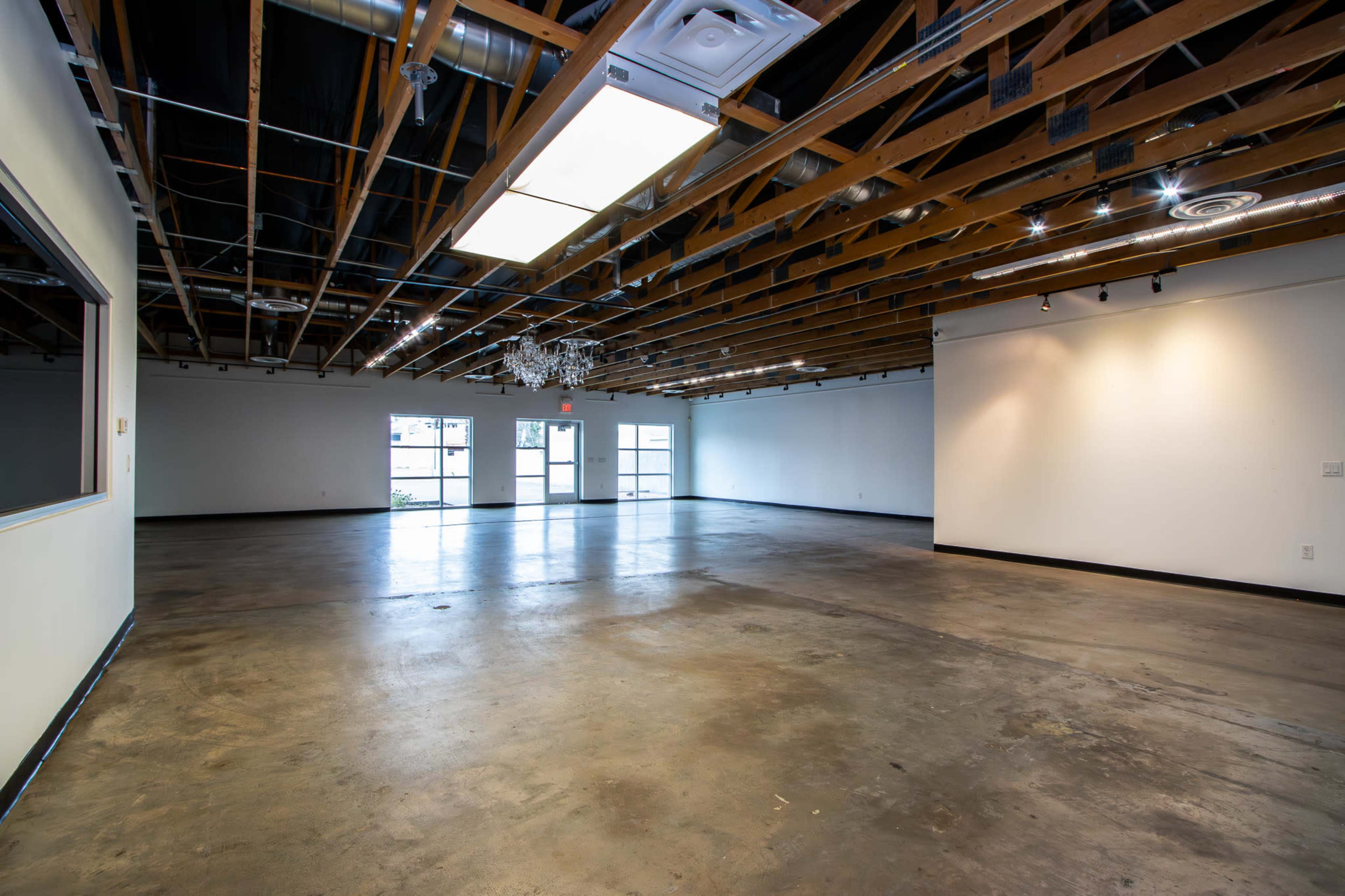An empty loft-like space with exposed wooden beams, concrete flooring, and large windows at one end.