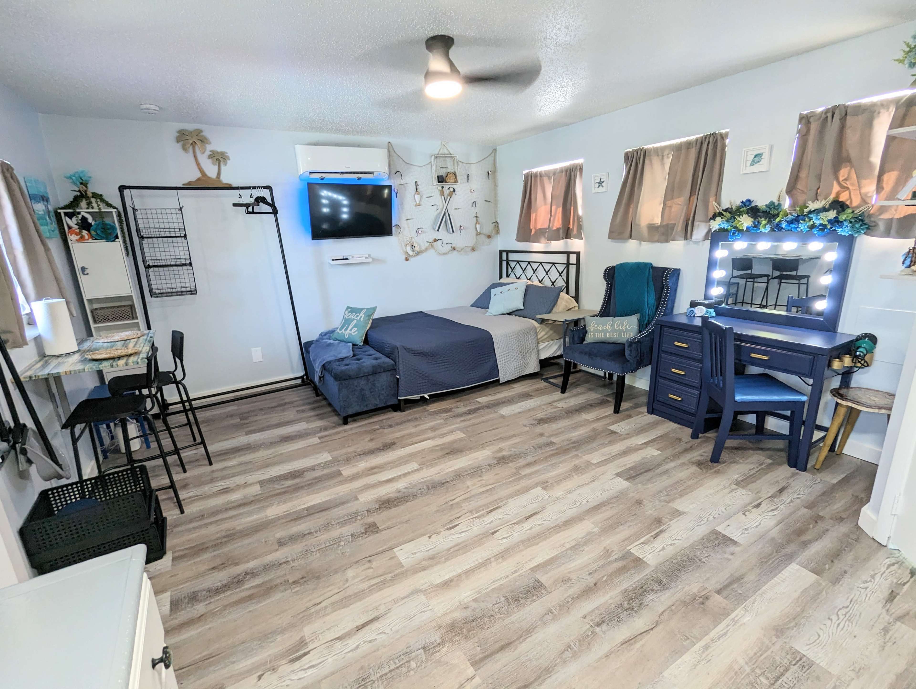 A well-organized bedroom featuring a bed, a desk with a mirror, a seating area, and decorative elements on the walls.