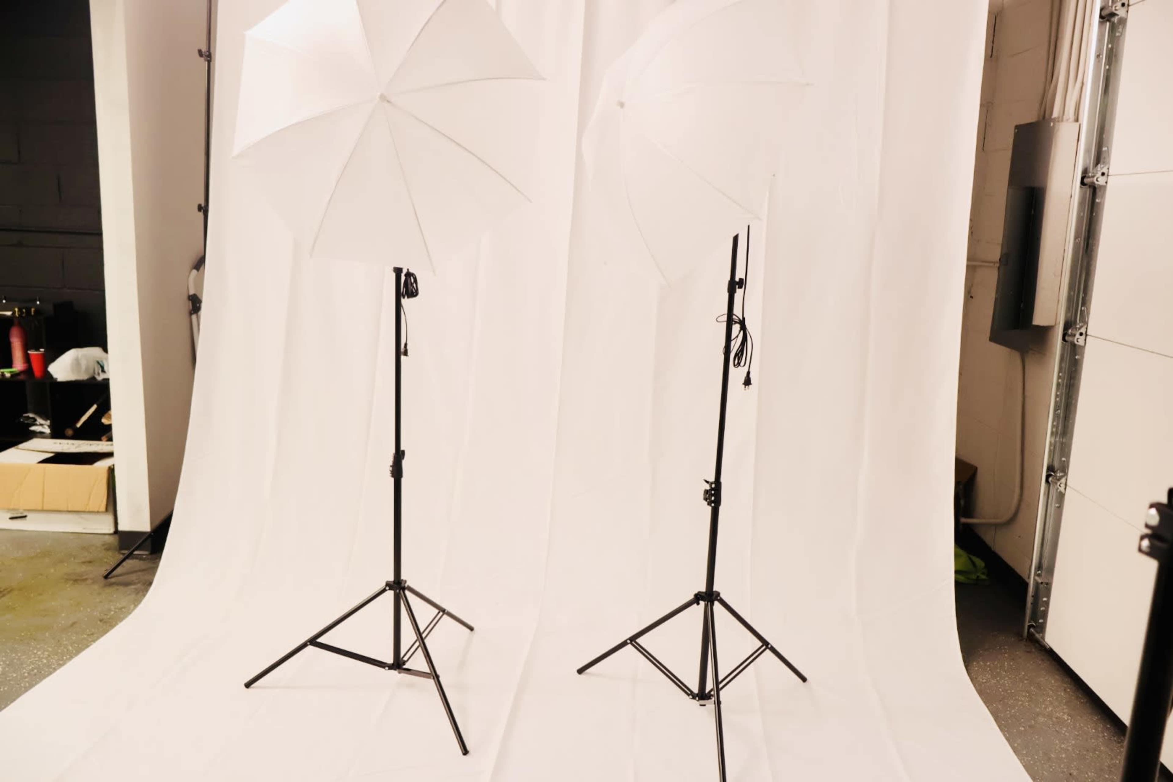 Two white photography umbrellas on black tripods positioned in front of a white backdrop.