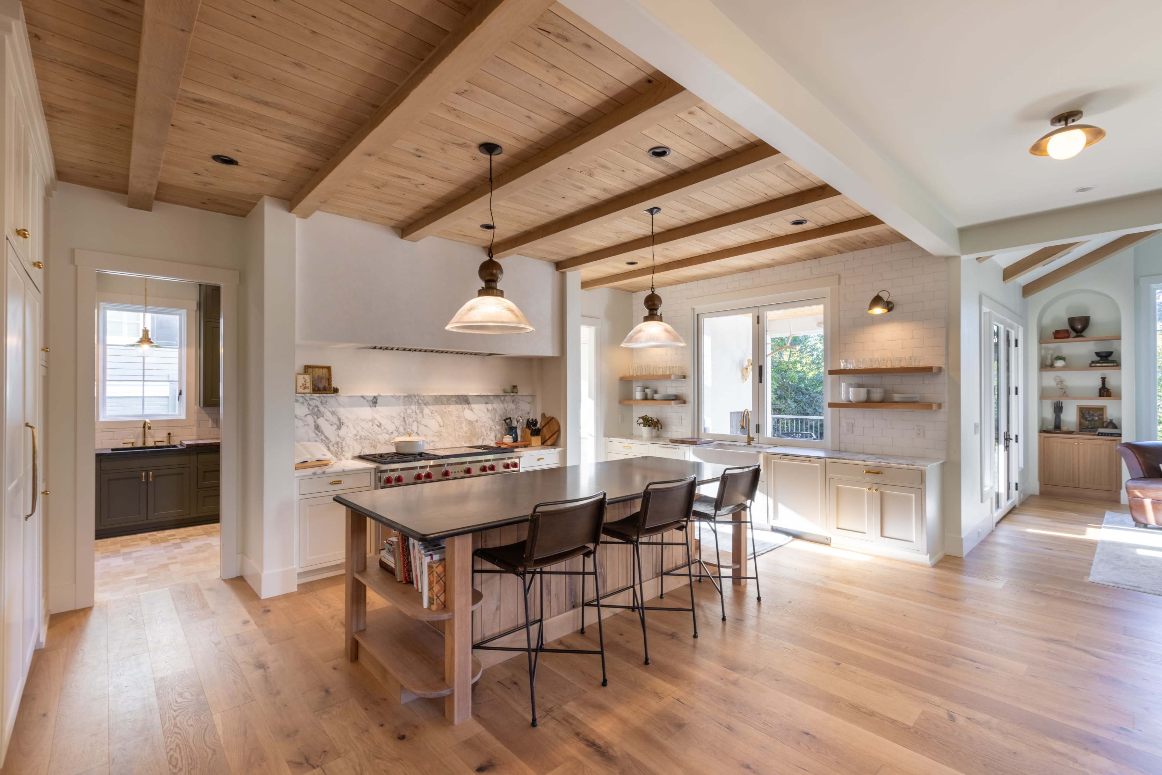 A spacious modern kitchen features a central island with seating, wooden beams on the ceiling, and marble countertops.