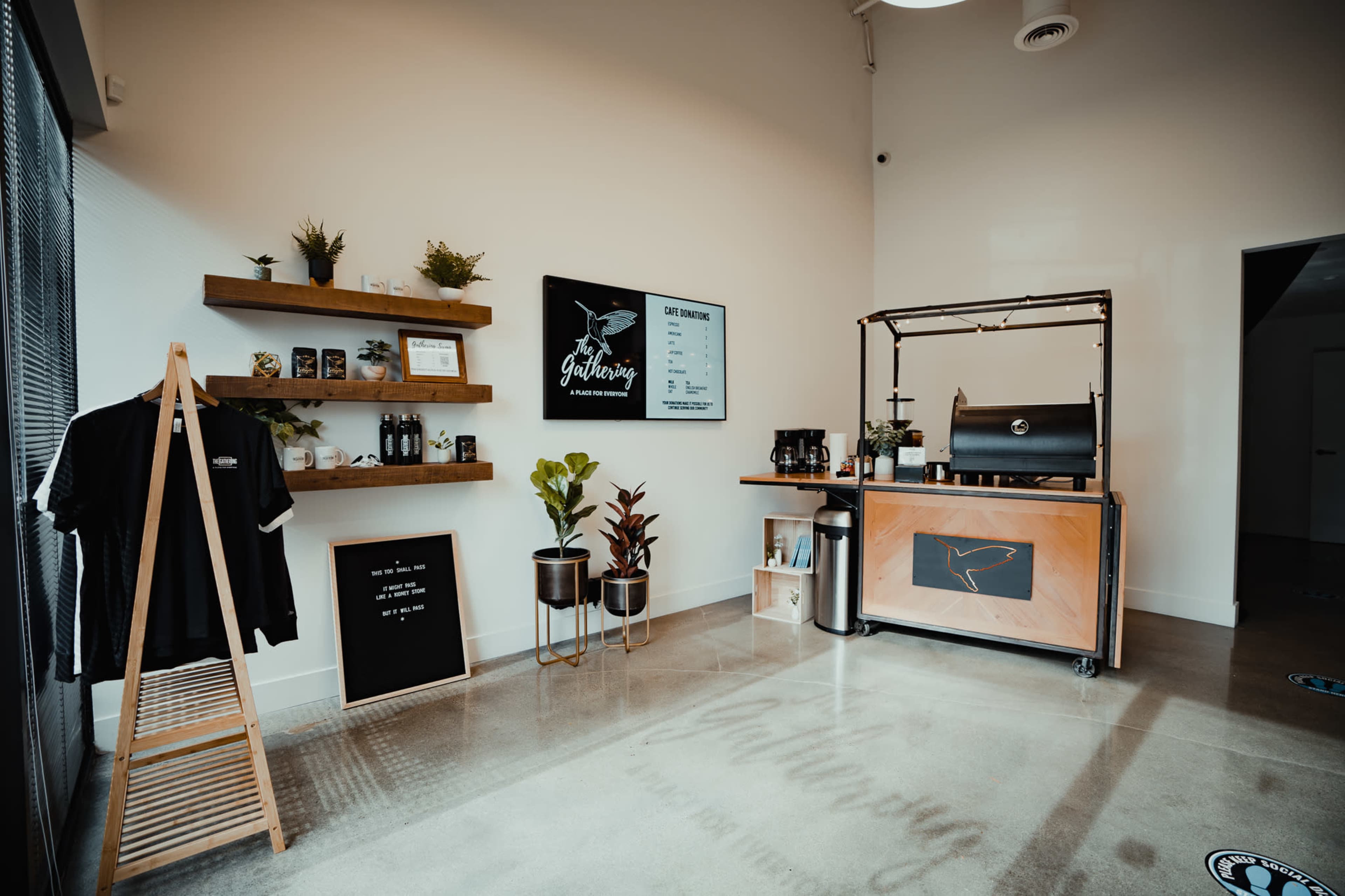A modern coffee shop interior featuring a wooden counter, shelves with decorative plants and merchandise, and a menu displayed on the wall.