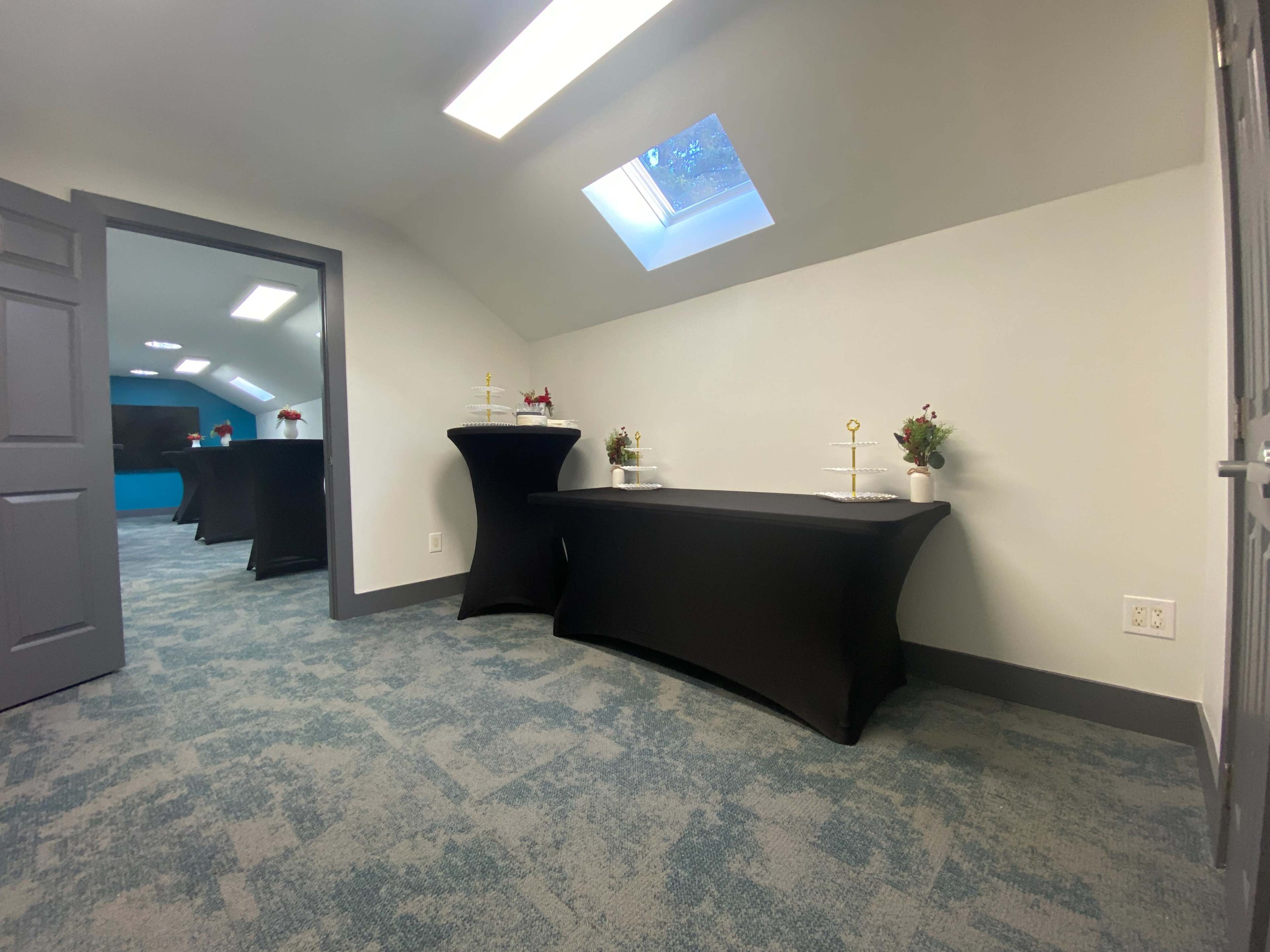 The image shows a well-lit meeting room with two black tablecloth-covered tables and a mirrored door in the background.