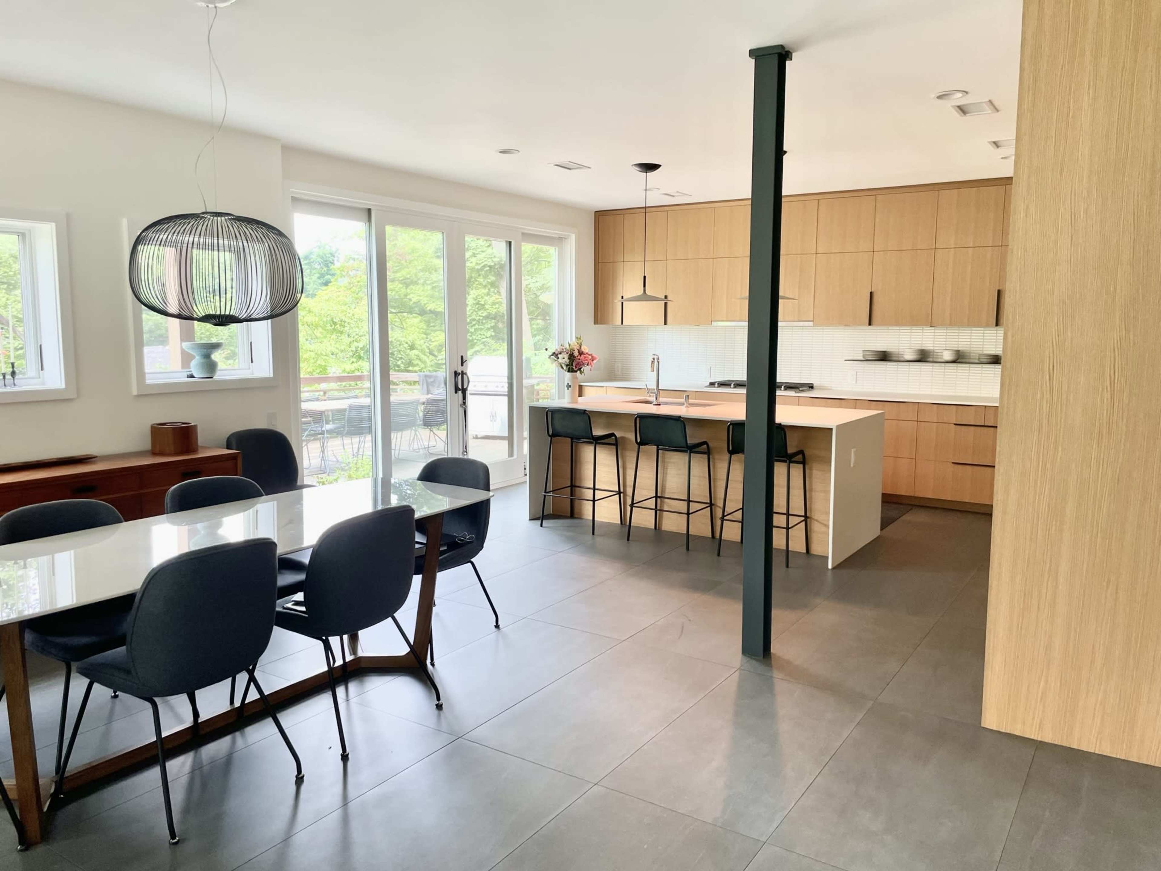 A modern kitchen and dining area features a light wood cabinetry, a large dining table, and bar stools at the kitchen counter.
