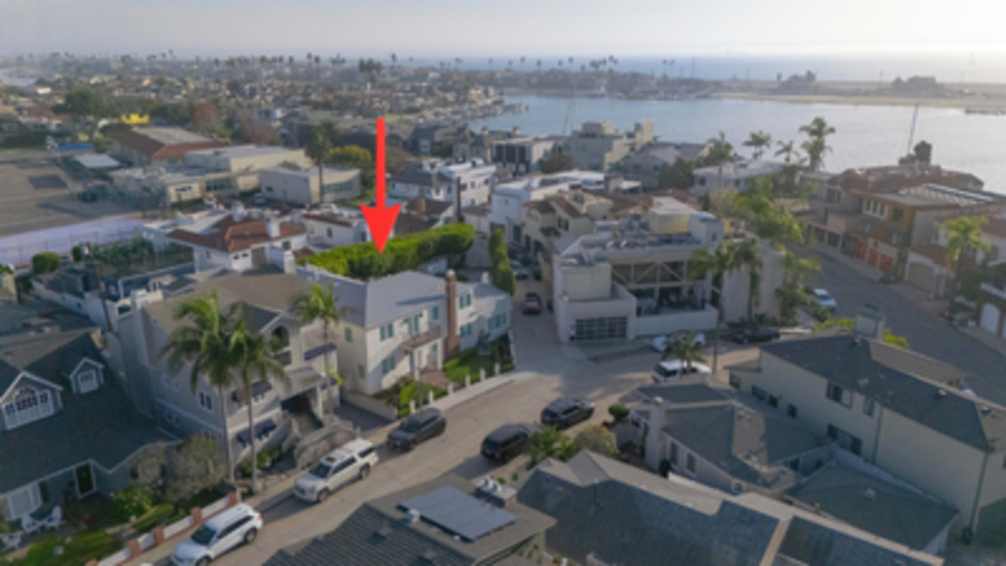 The image shows an aerial view of a coastal neighborhood with houses, palm trees, and water in the background.