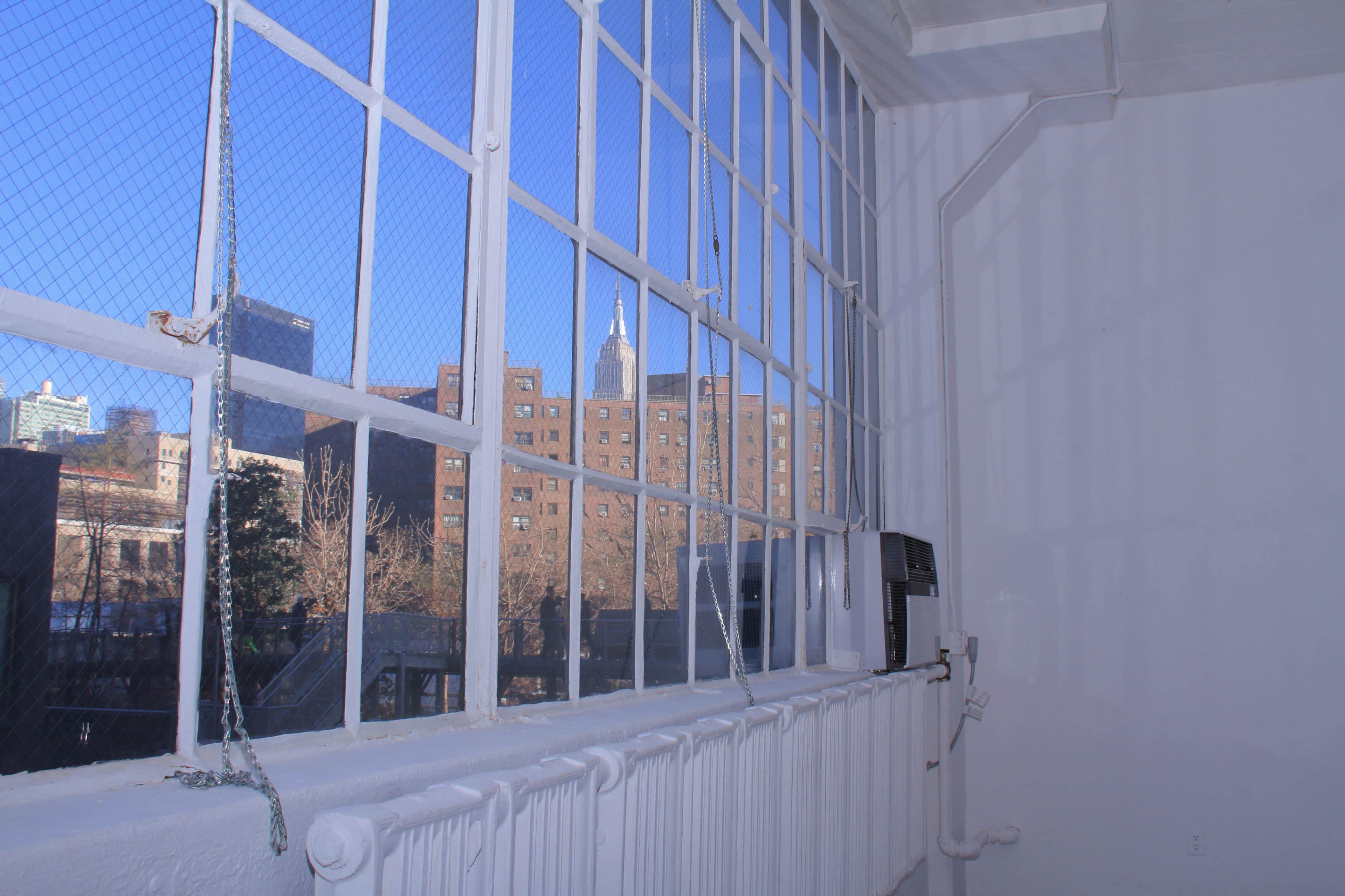 The image shows a white-walled interior space with large windows overlooking a cityscape featuring a tower in the background.