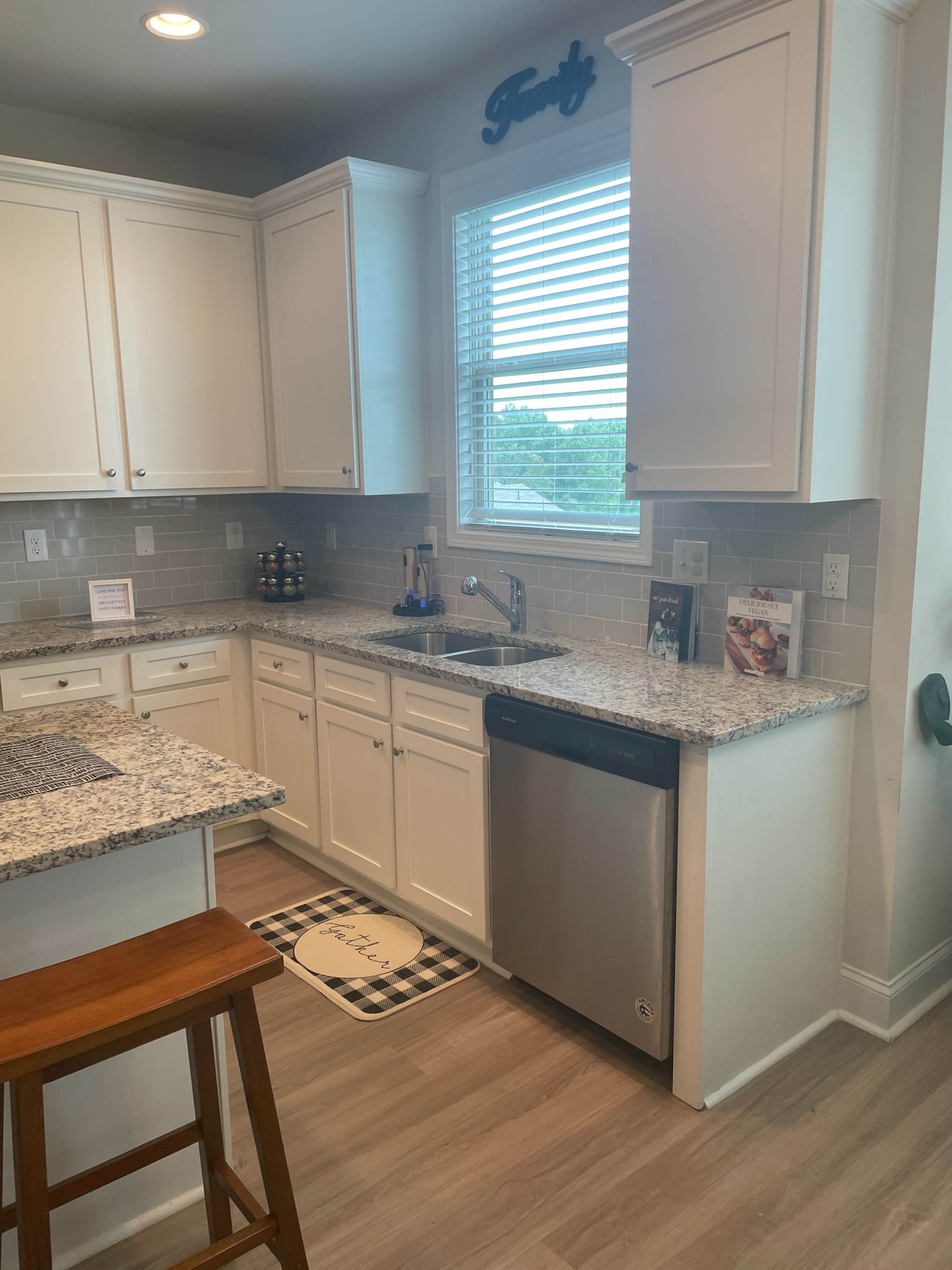A modern kitchen with white cabinets, a granite countertop, a sink under a window, and a dishwashing appliance.