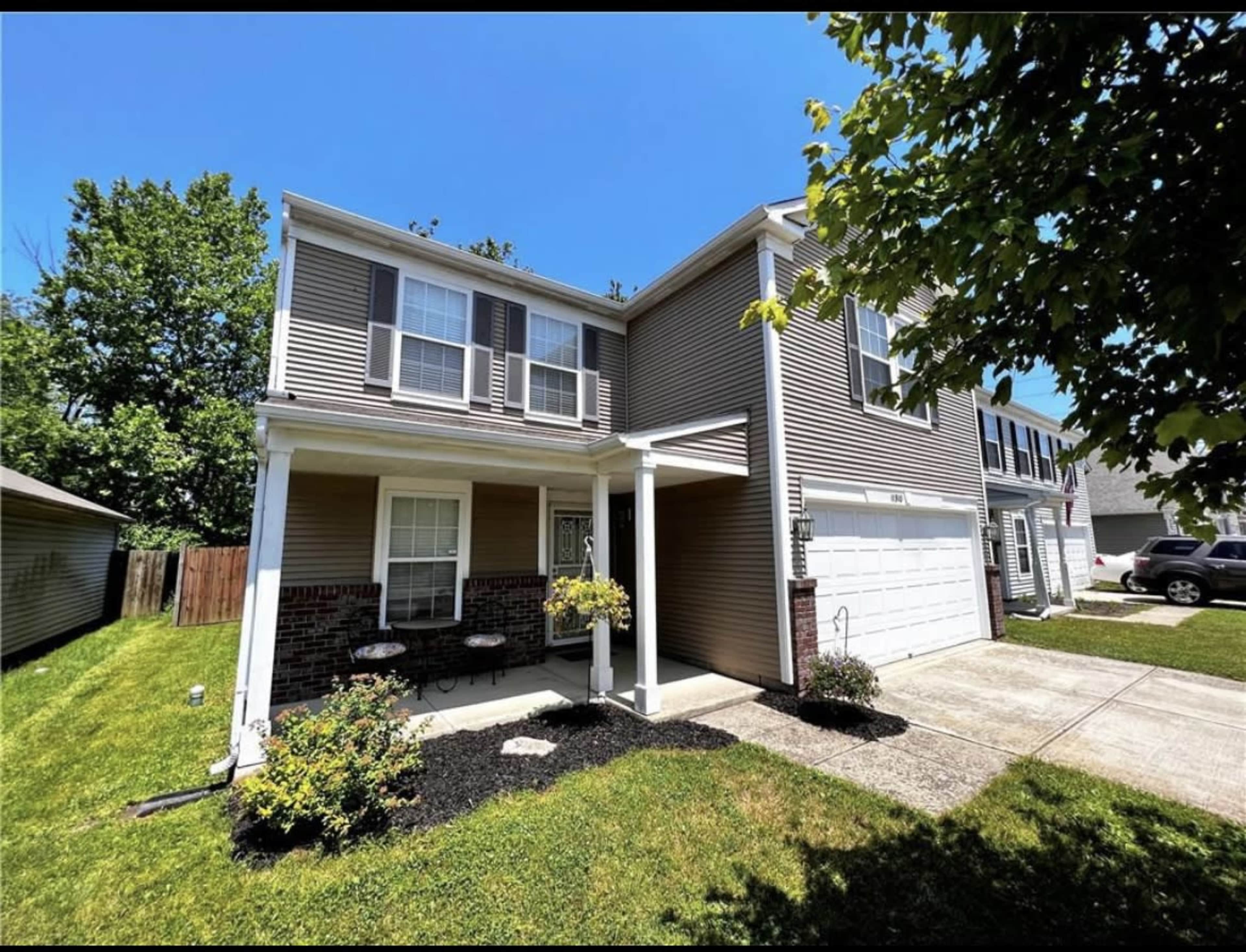 A two-story house with a covered porch, a garage, and a neat lawn surrounded by trees.