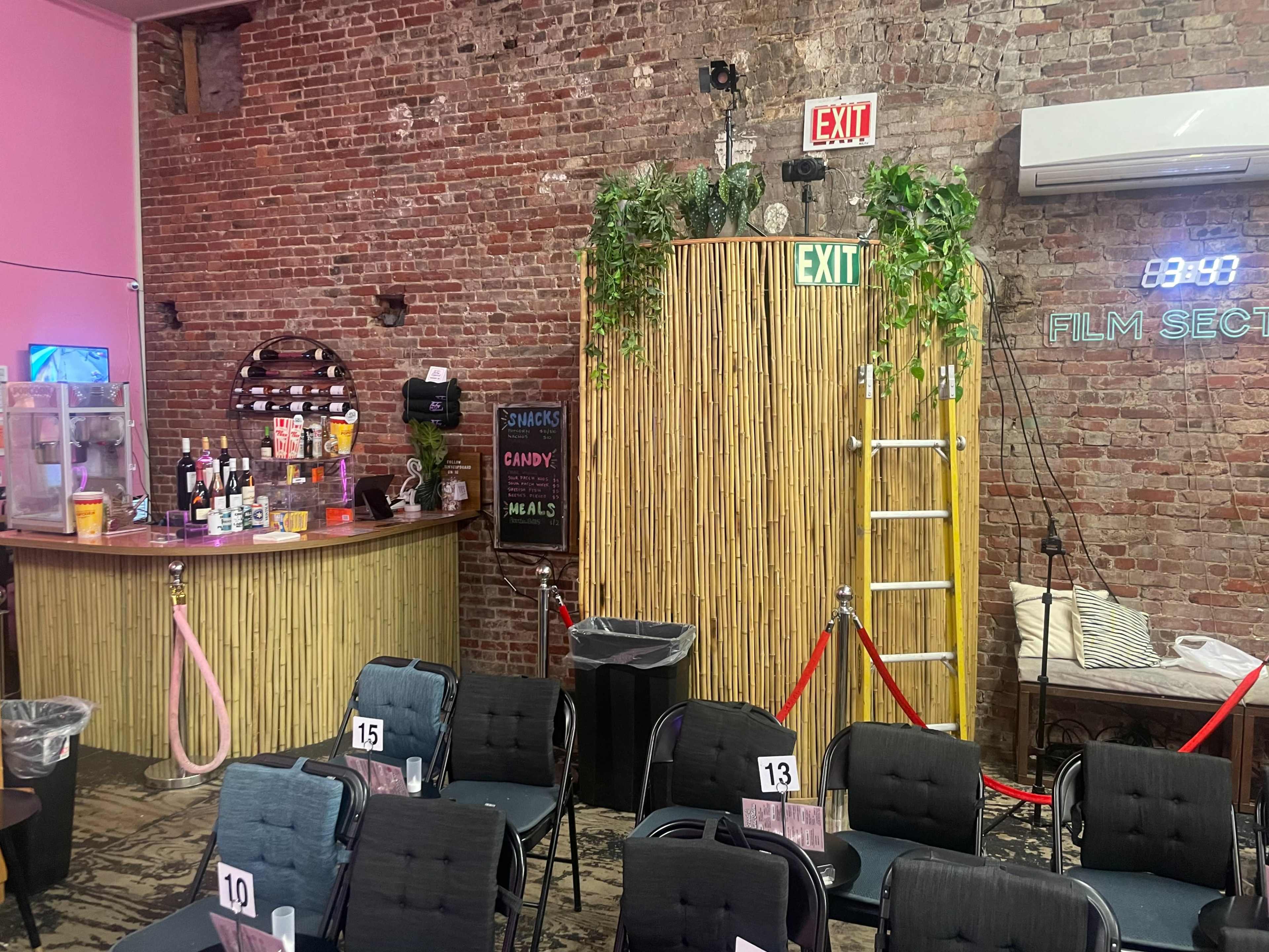A rustic venue with a bar area, a bamboo partition with greenery, and rows of chairs set up for an event.