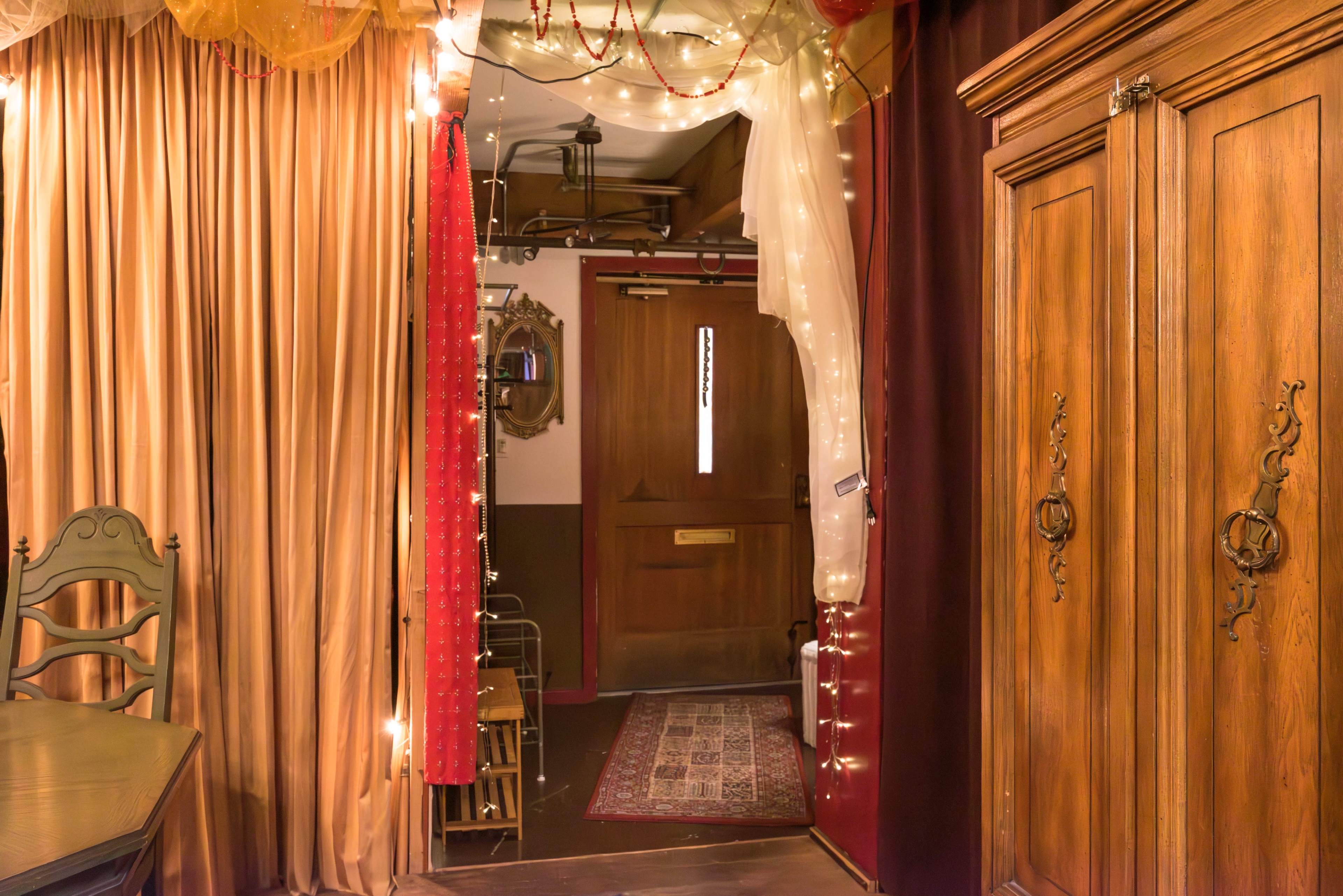 A cozy hallway adorned with draped curtains and string lights, leading to a wooden door.