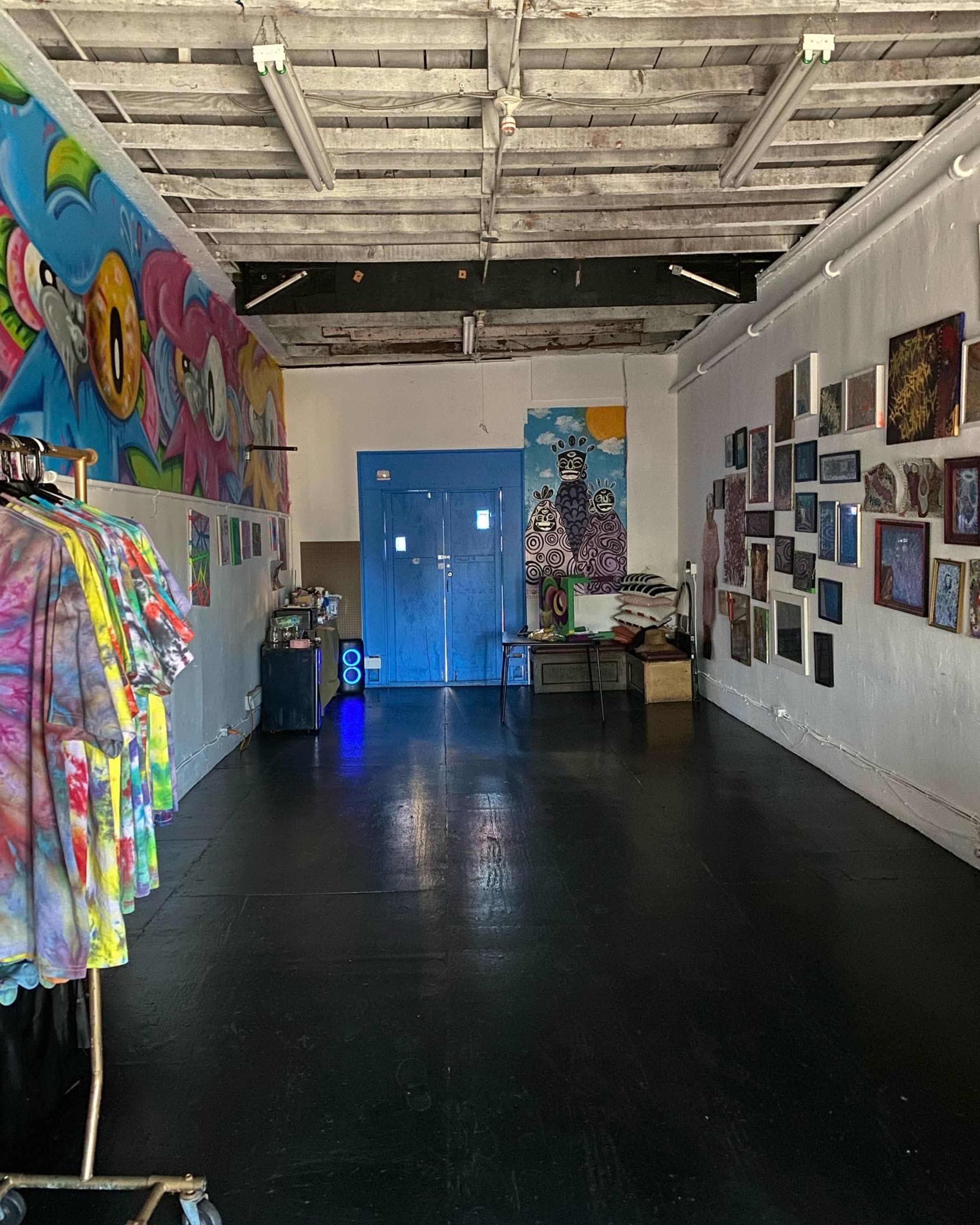 The image shows a spacious, brightly colored room with artistic murals on the walls, a blue door at the end, and clothing racks on one side.