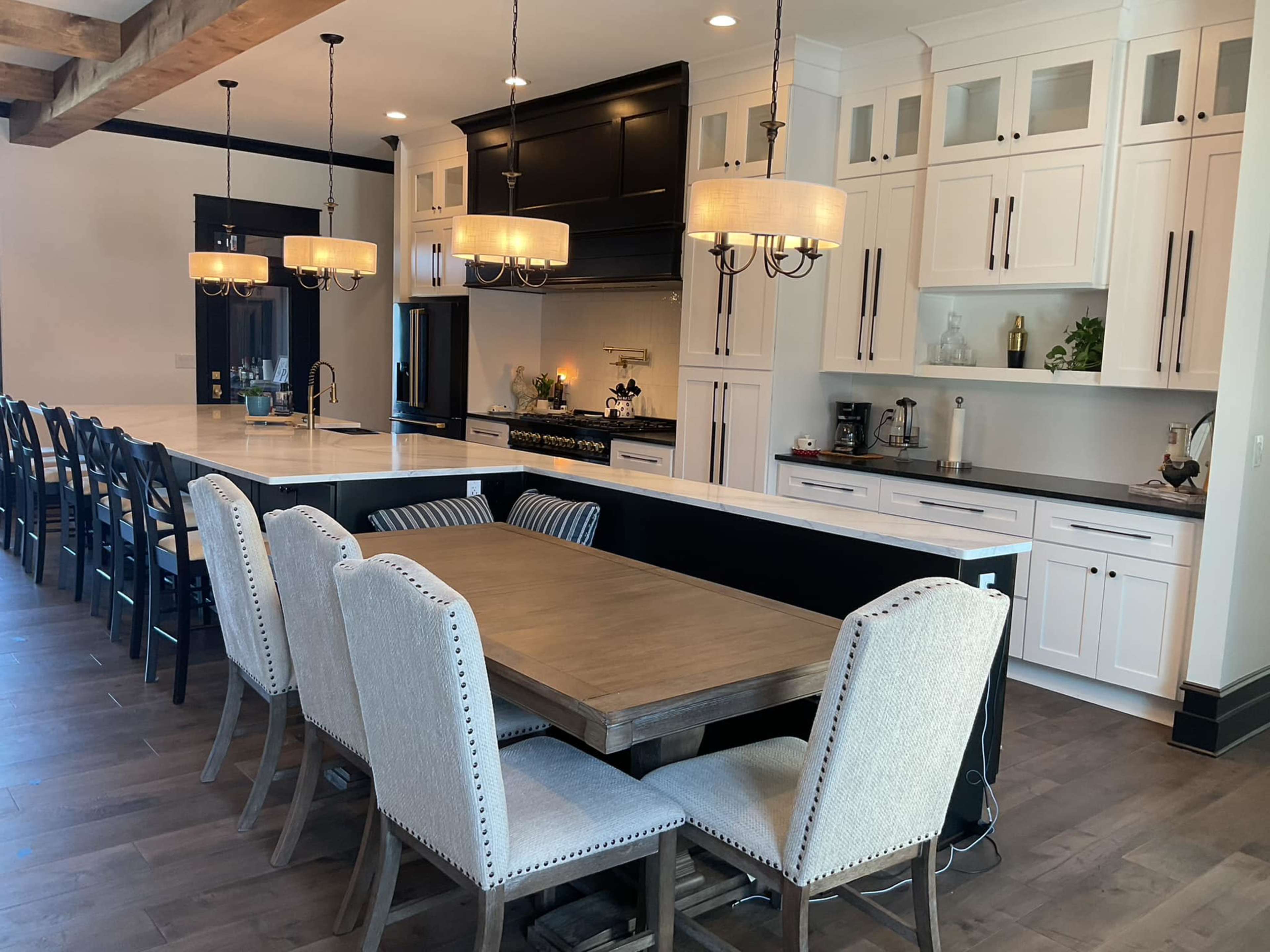 A modern kitchen features a central island with bar seating, a wooden dining table surrounded by upholstered chairs, and pendant lighting above.